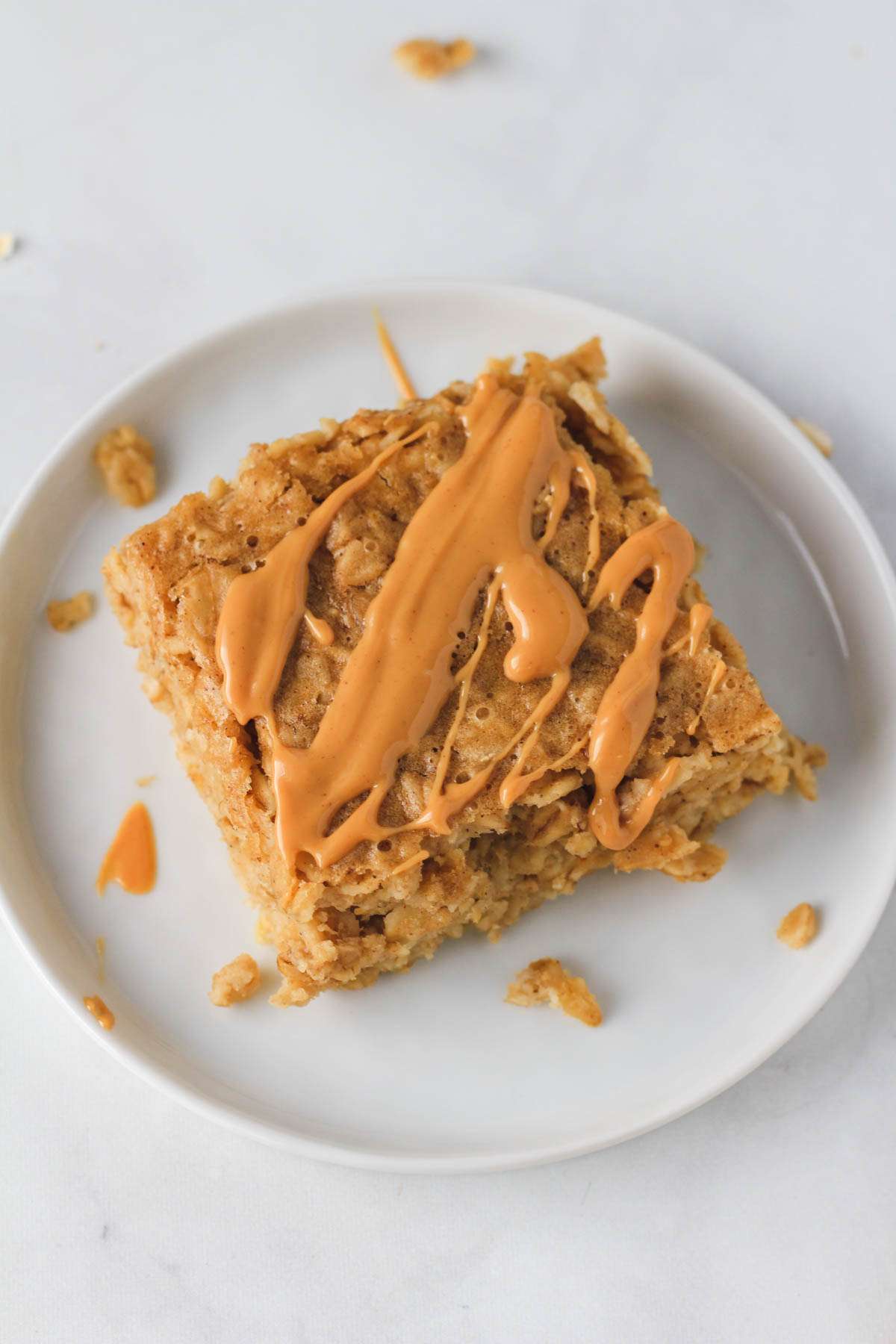 A small white plate with a square of baked oatmeal topped with melted peanut butter.