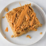 A close up of a white plate with one peanut butter oatmeal square topped with peanut butter.