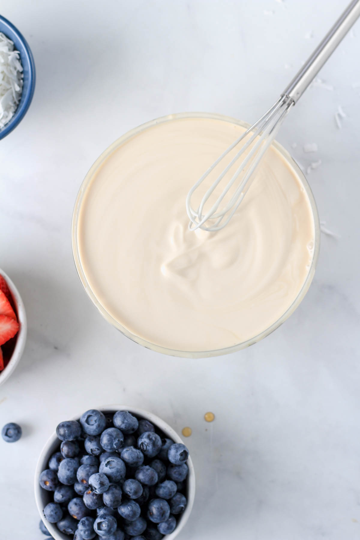 A small glass bowl with the vegan yogurt mixture and a small wire whisk.