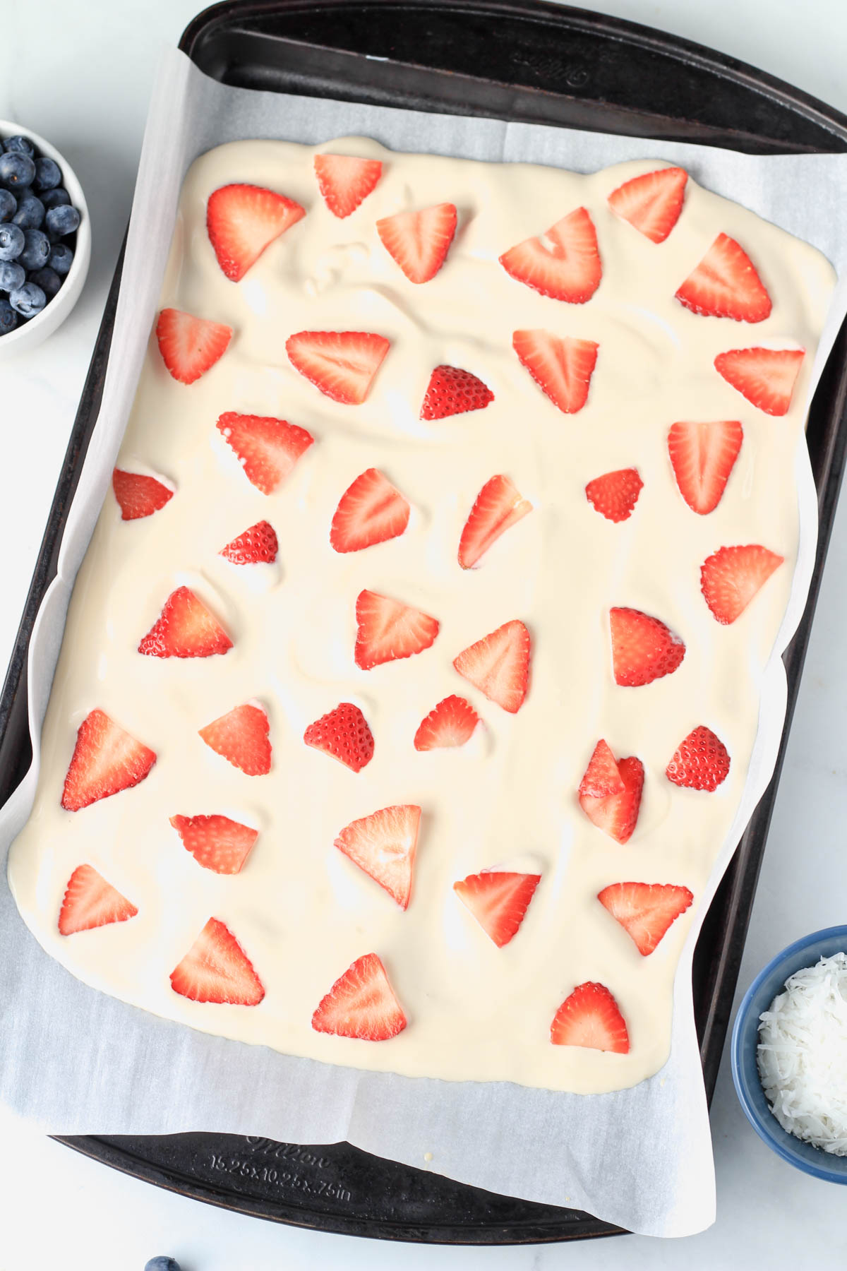 A parchment paper lined cookie sheet with the vegan yogurt mixture spread out and topped with sliced strawberry.