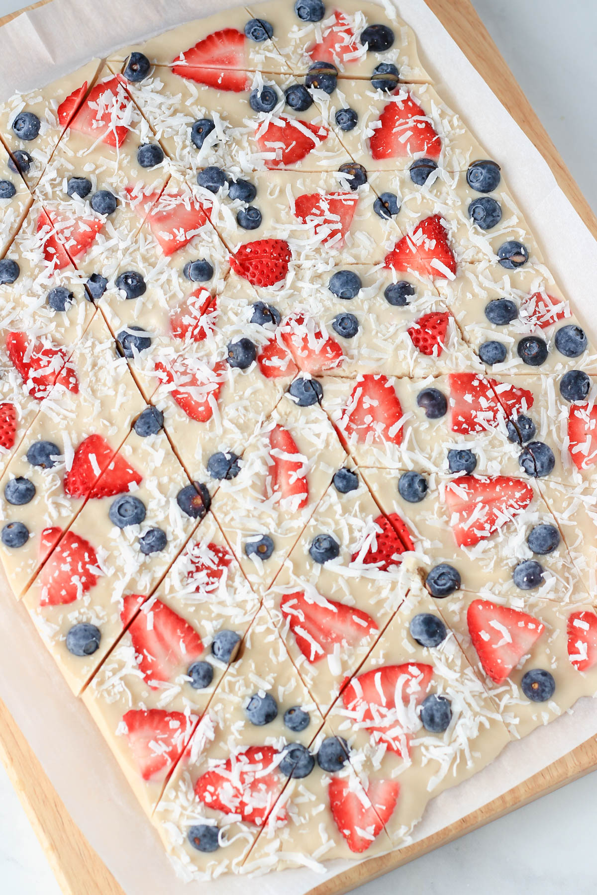 A wooden cutting board lined with parchment paper and topped with sliced frozen yogurt bark.