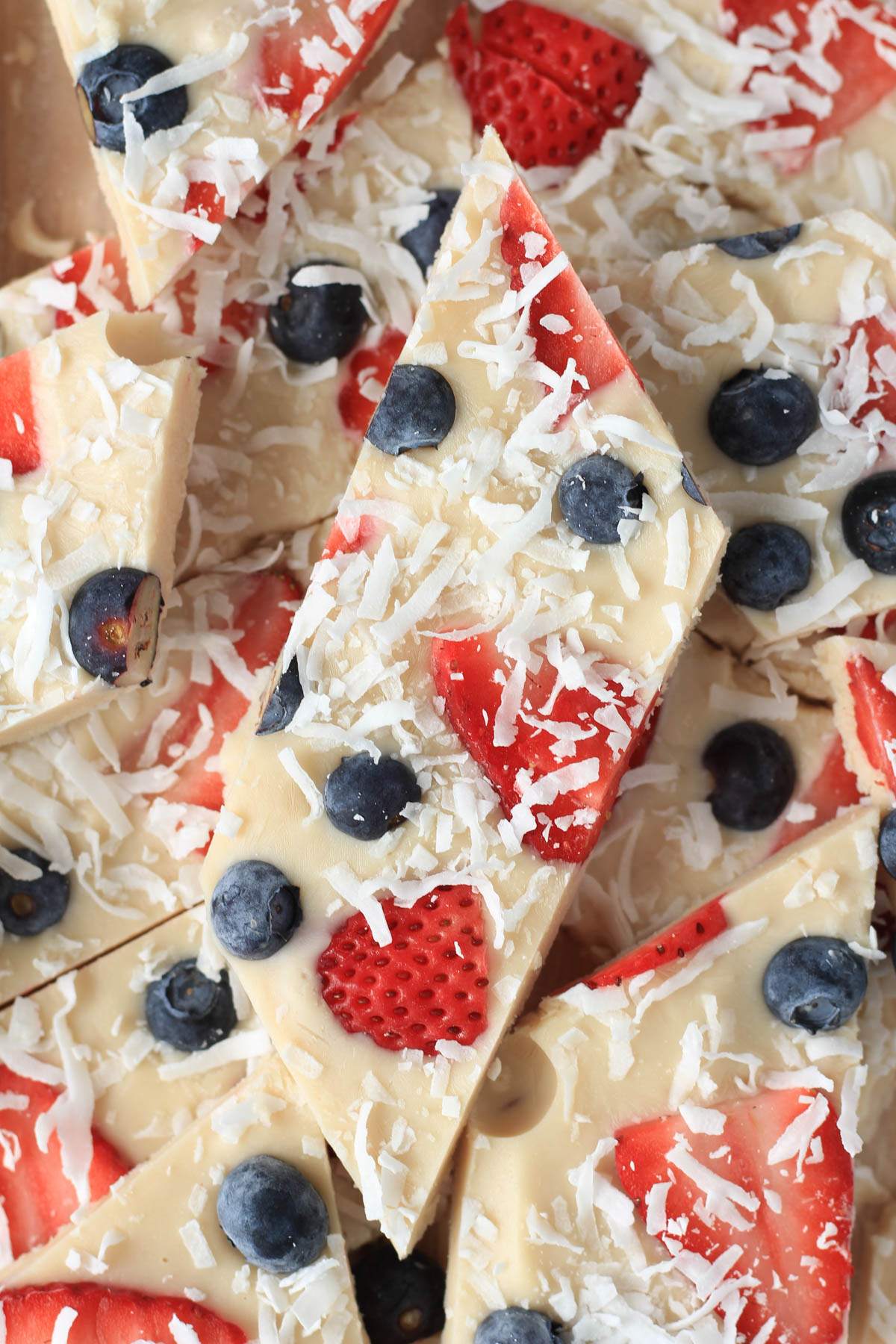 A close up of a slice of vegan frozen yogurt bark with strawberry, blueberry, and shredded coconut.