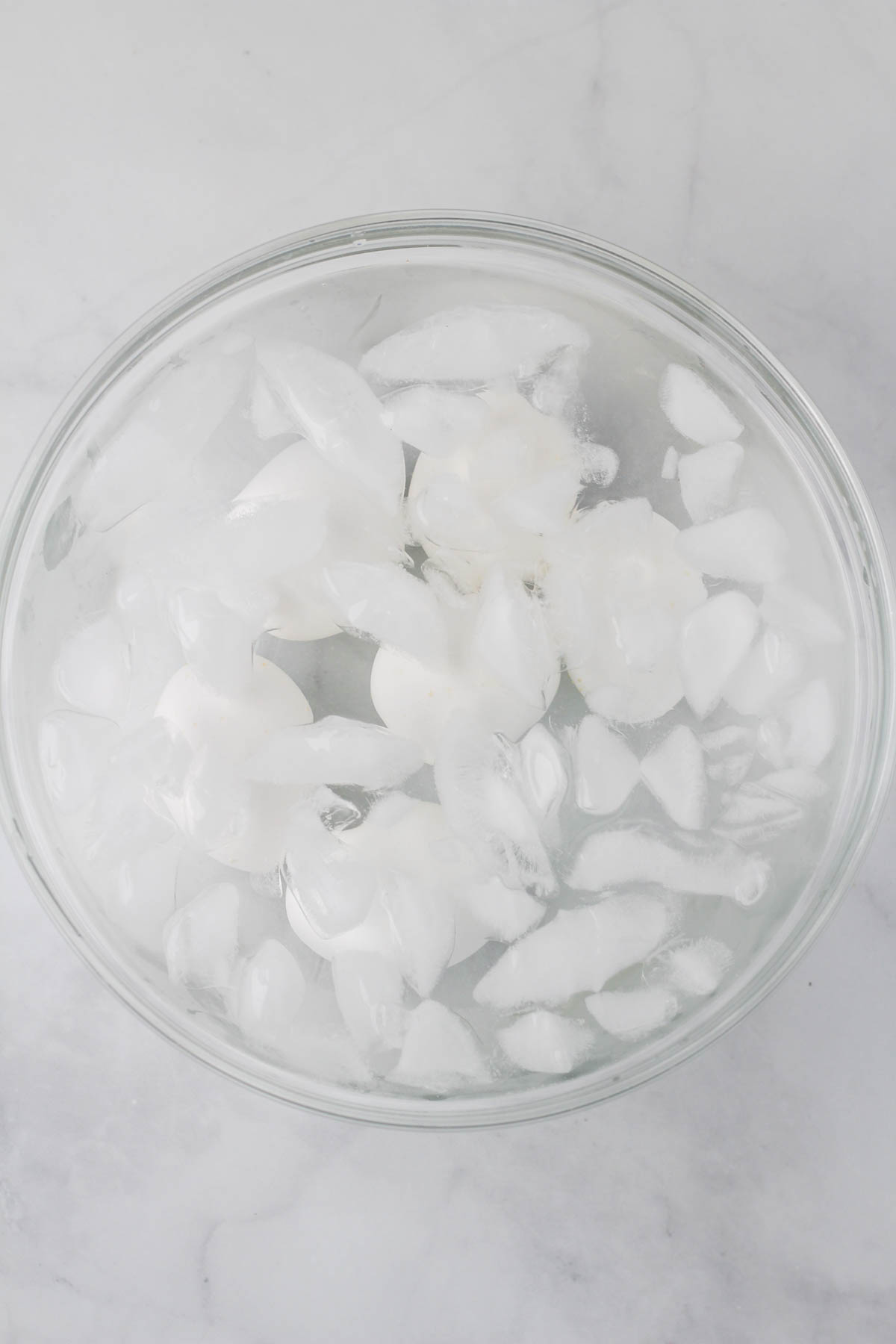 A glass bowl with an ice bath and 6 hard boiled eggs.