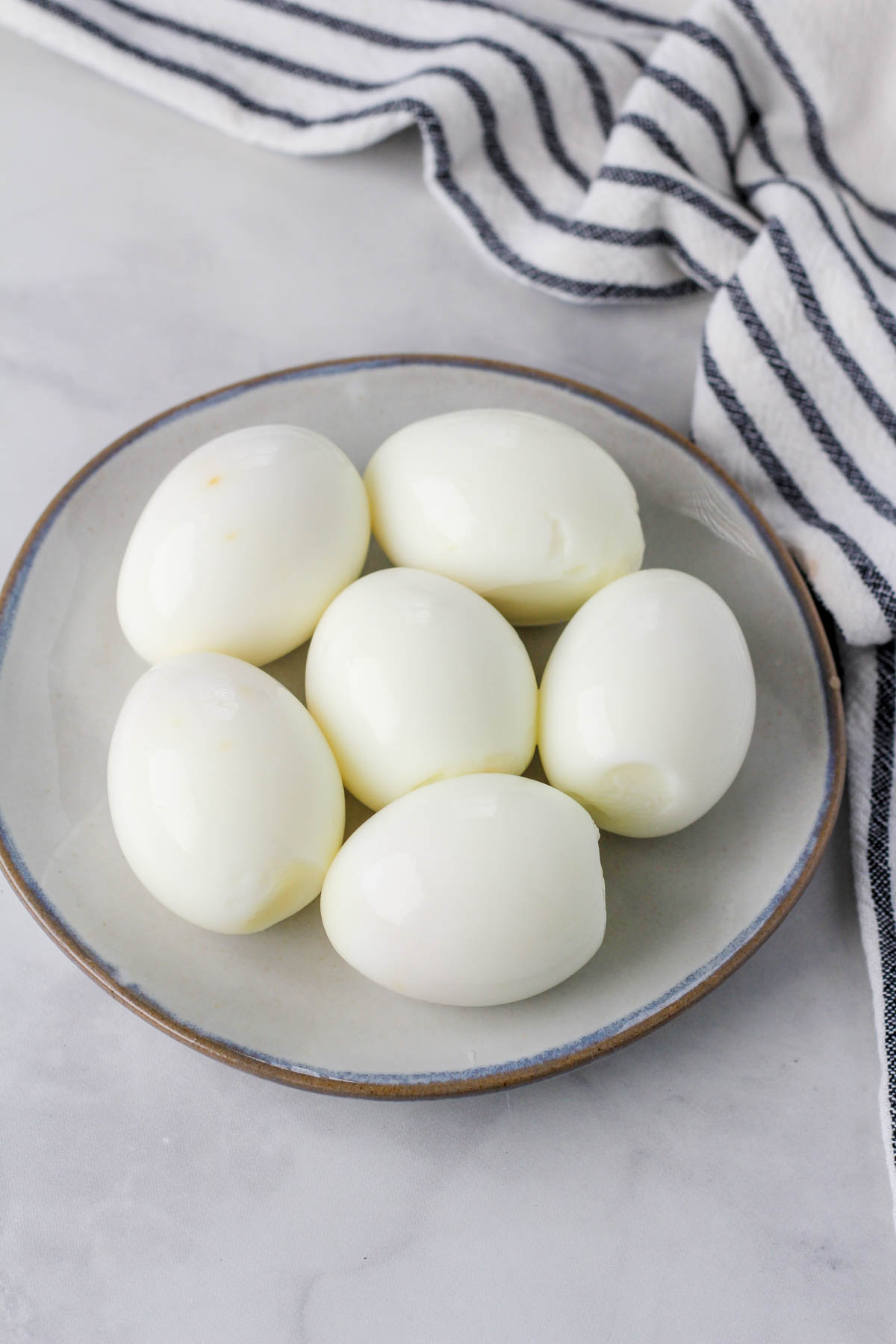 A small plate on a white counter with 6 peeled hard boiled eggs.