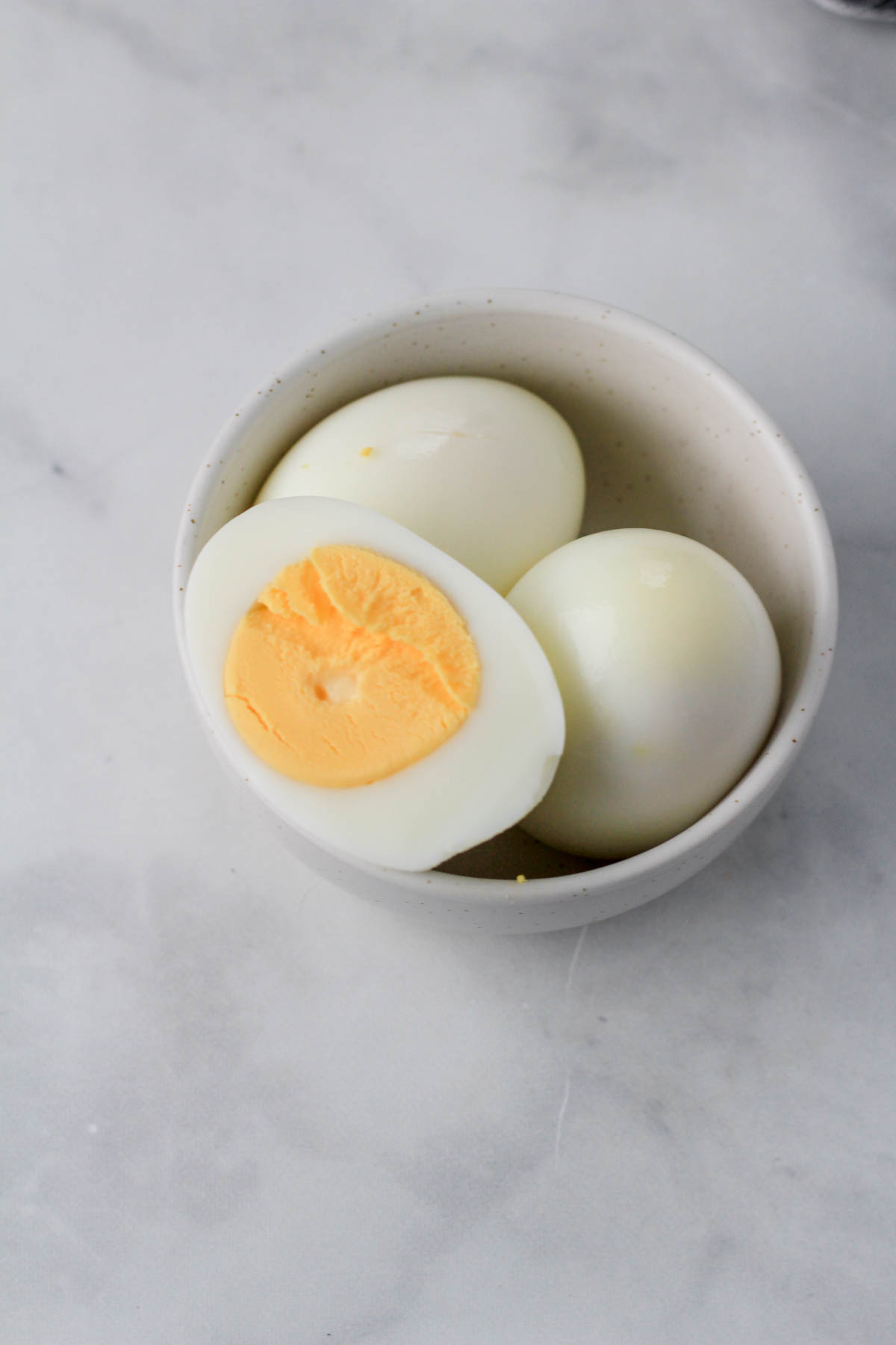 A small white bowl with three hard boiled eggs and one sliced in half to show the center yolk.