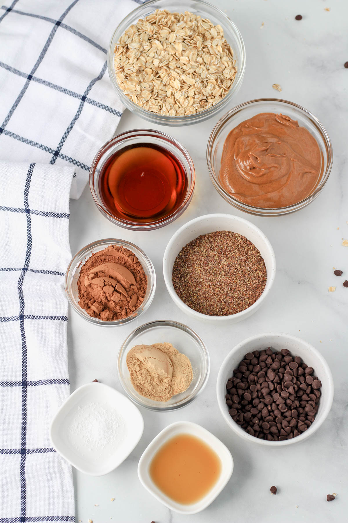 Ingredients for vegan chocolate almond lactation bites on a white counter with a blue and white towel to the left.