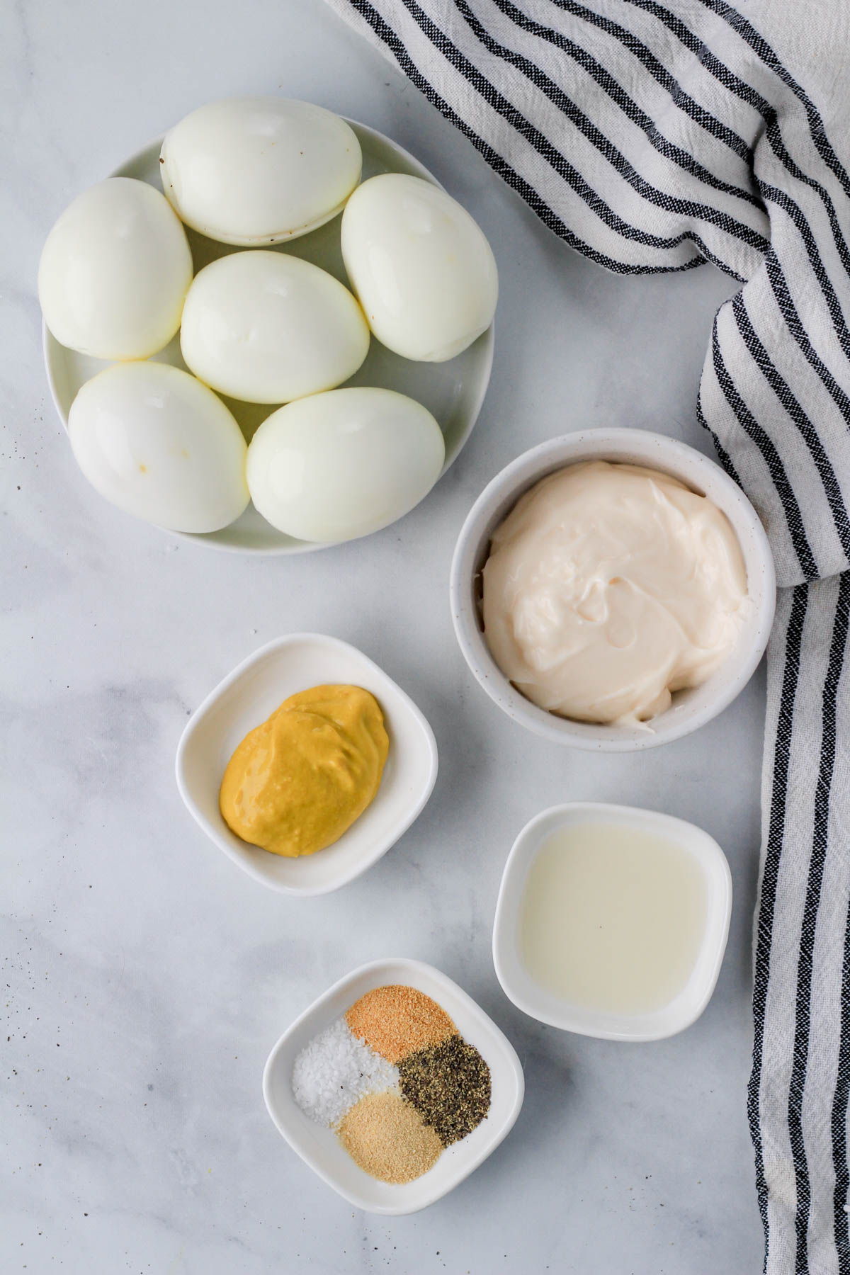 Ingredients for egg salad on a white counter with a blue and white striped dish towel to the right.