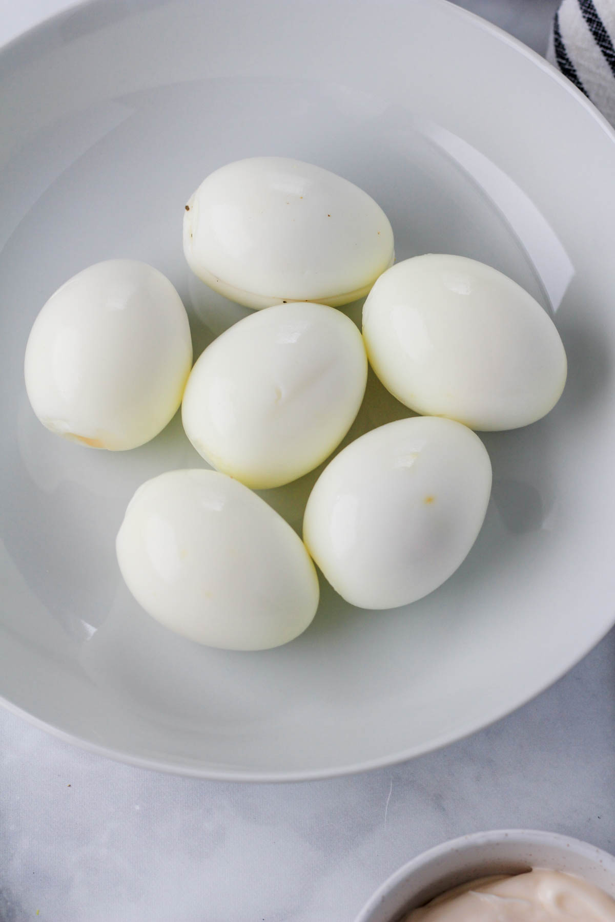 A white bowl with hard boiled eggs.
