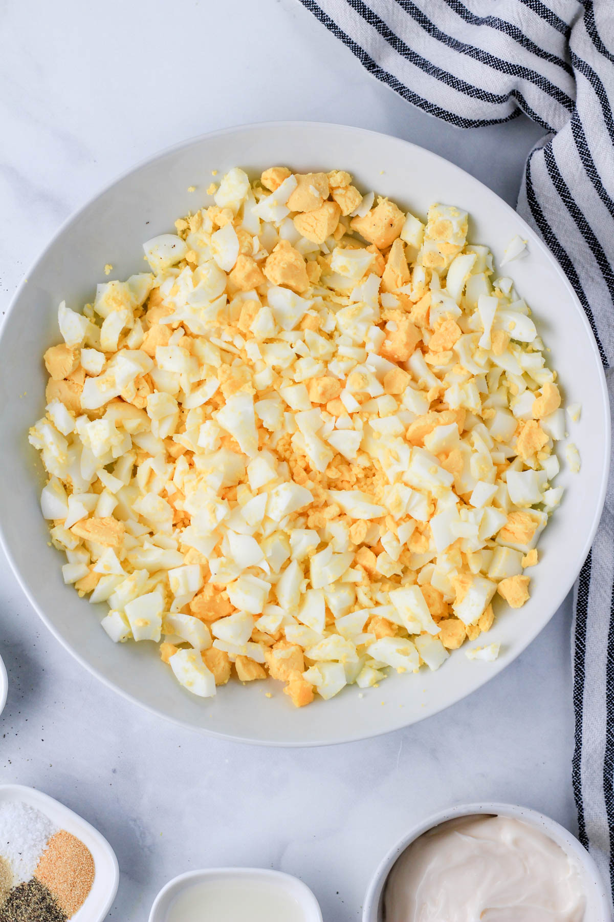 A white bowl with chopped hard boiled eggs next to a white a blue dish towel.