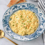 A white and blue serving bowl of classic egg salad topped with green onion.