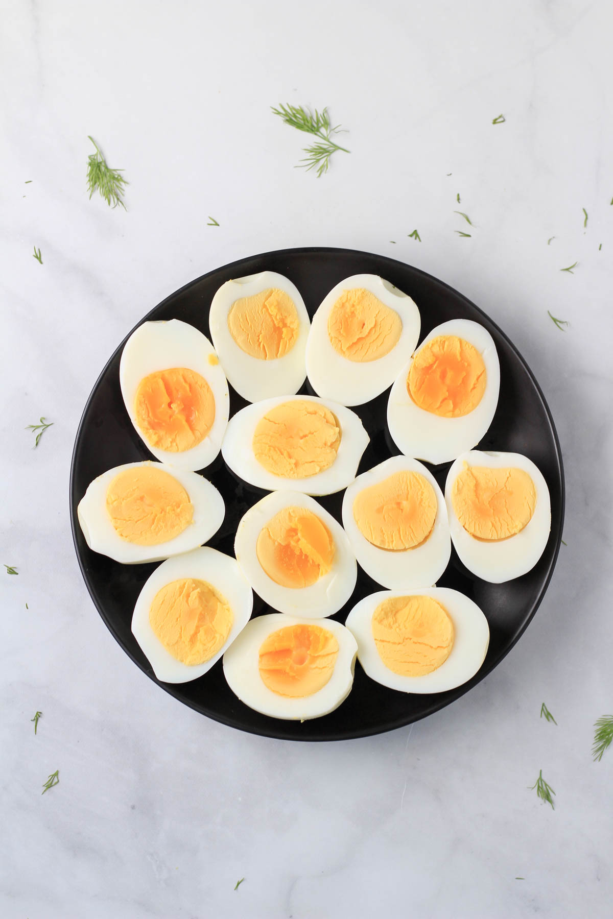 A black plate with hard boiled eggs sliced in half to exposed the cooked egg.