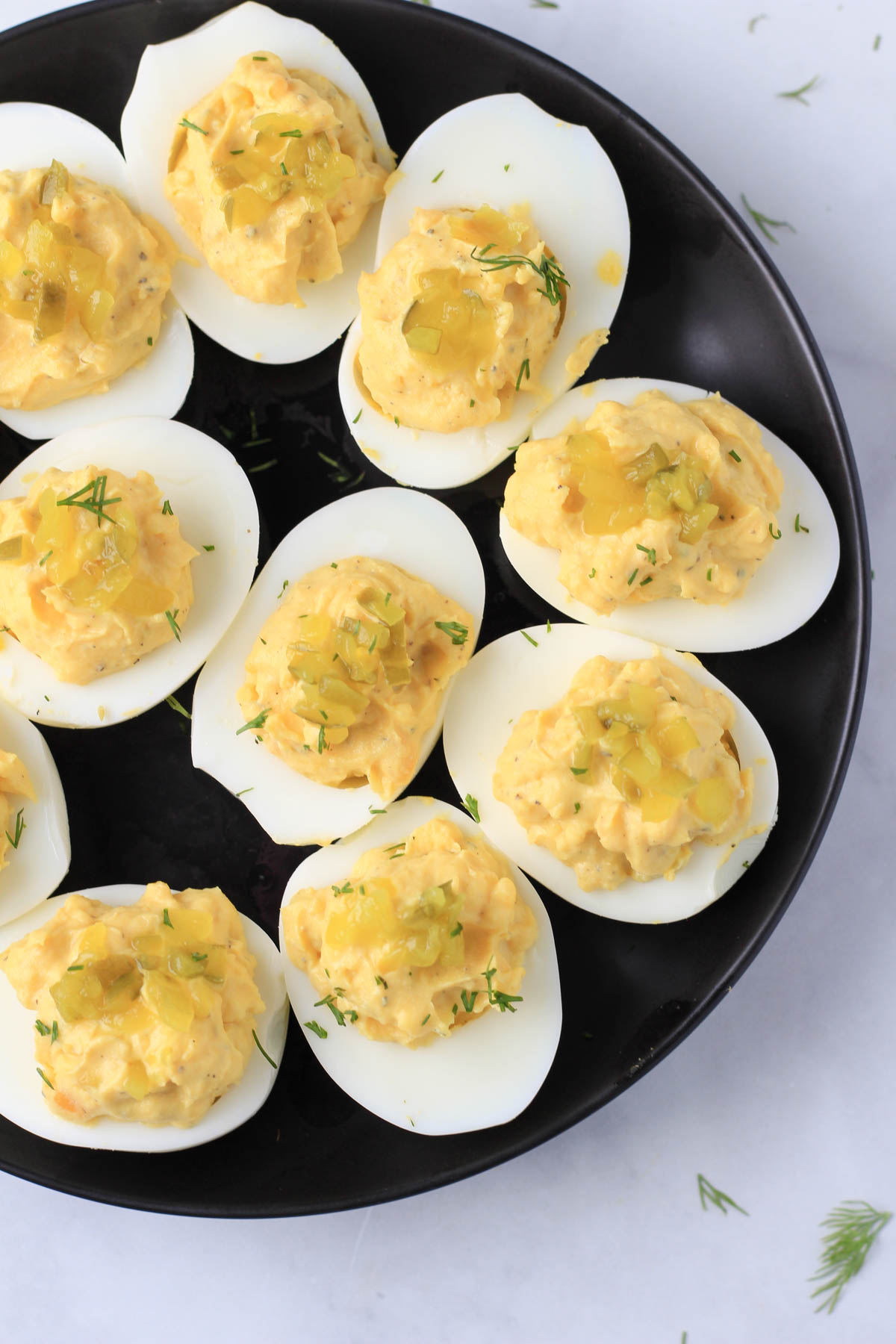 Deviled eggs on a black plate with dill and relish on top.