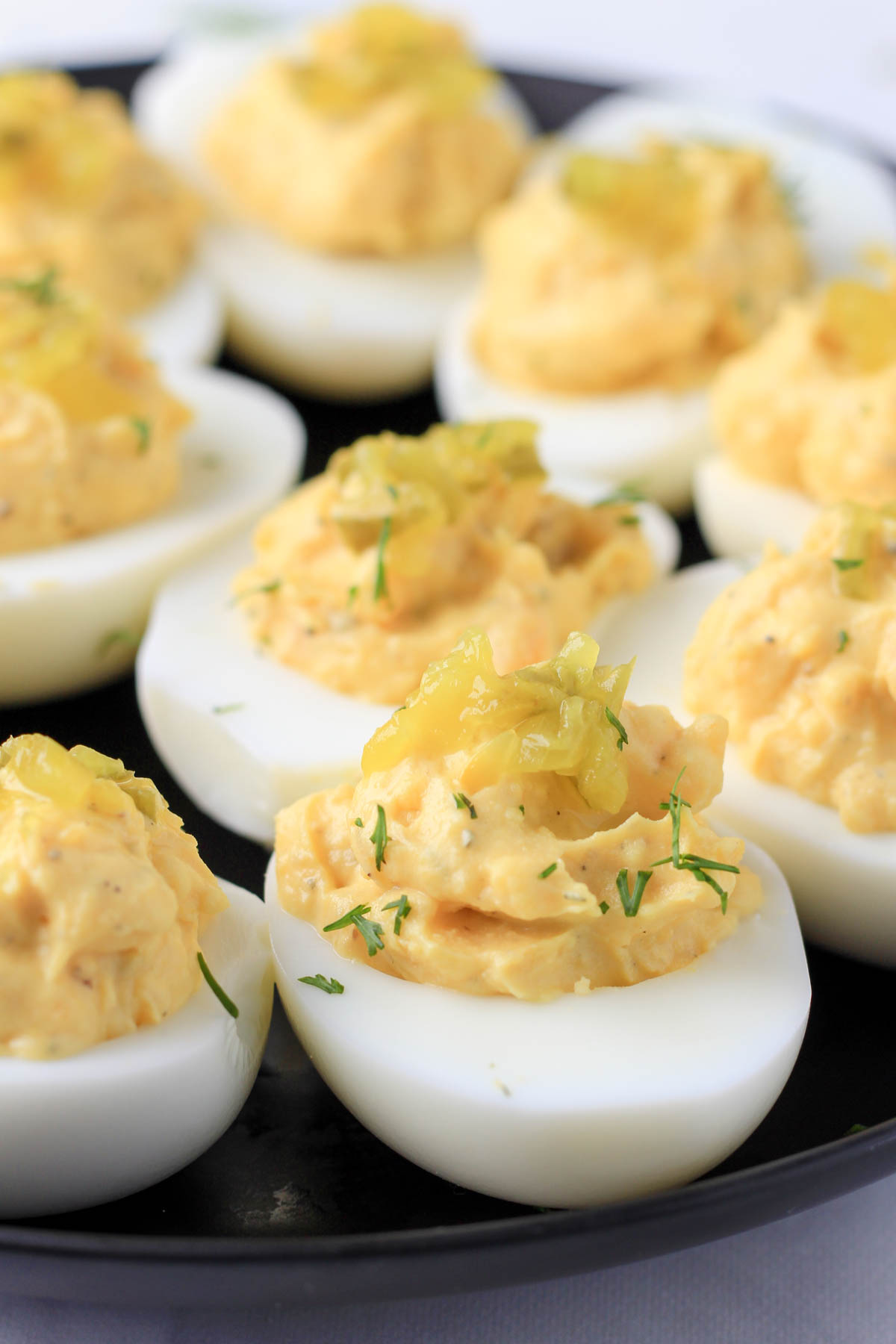 Dill pickle deviled eggs on a black plate topped with fresh dill and pickle relish.