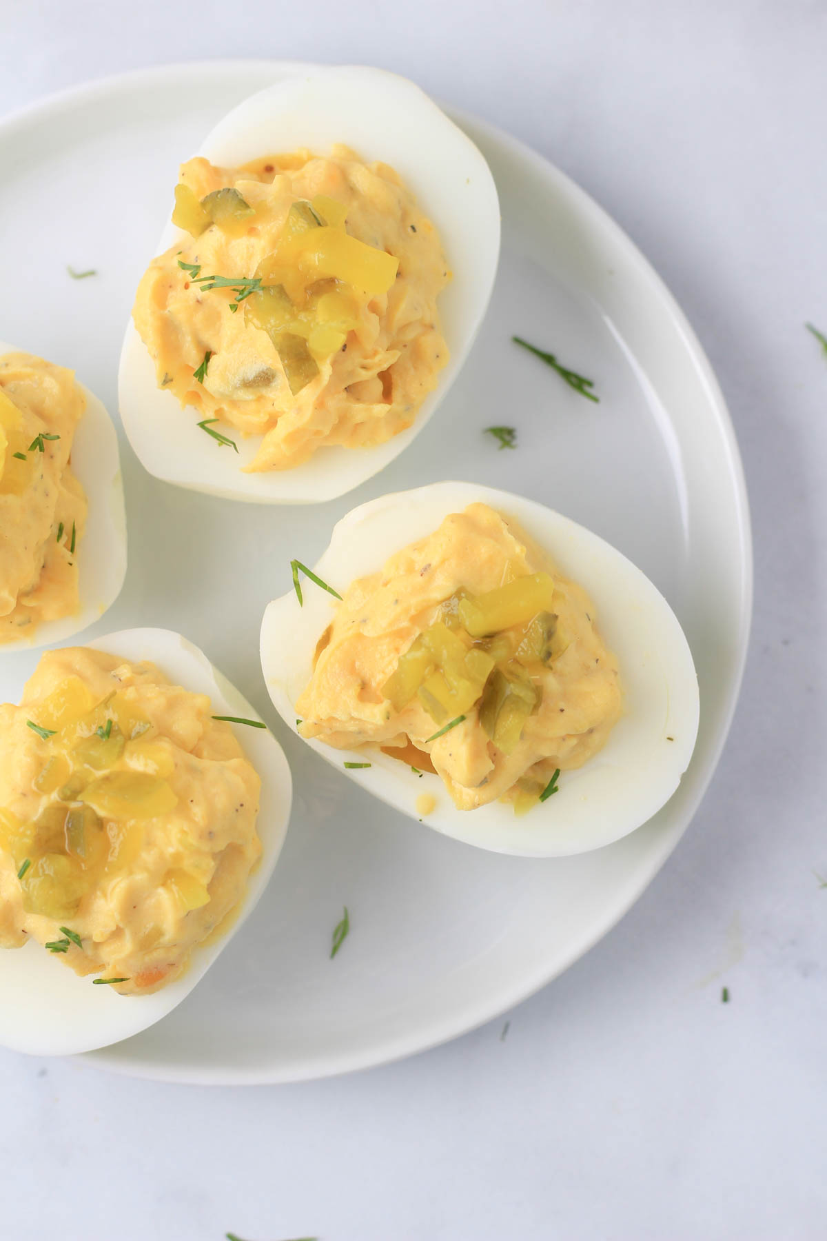 A top down photo of dill pickle deviled eggs on a small white plate.