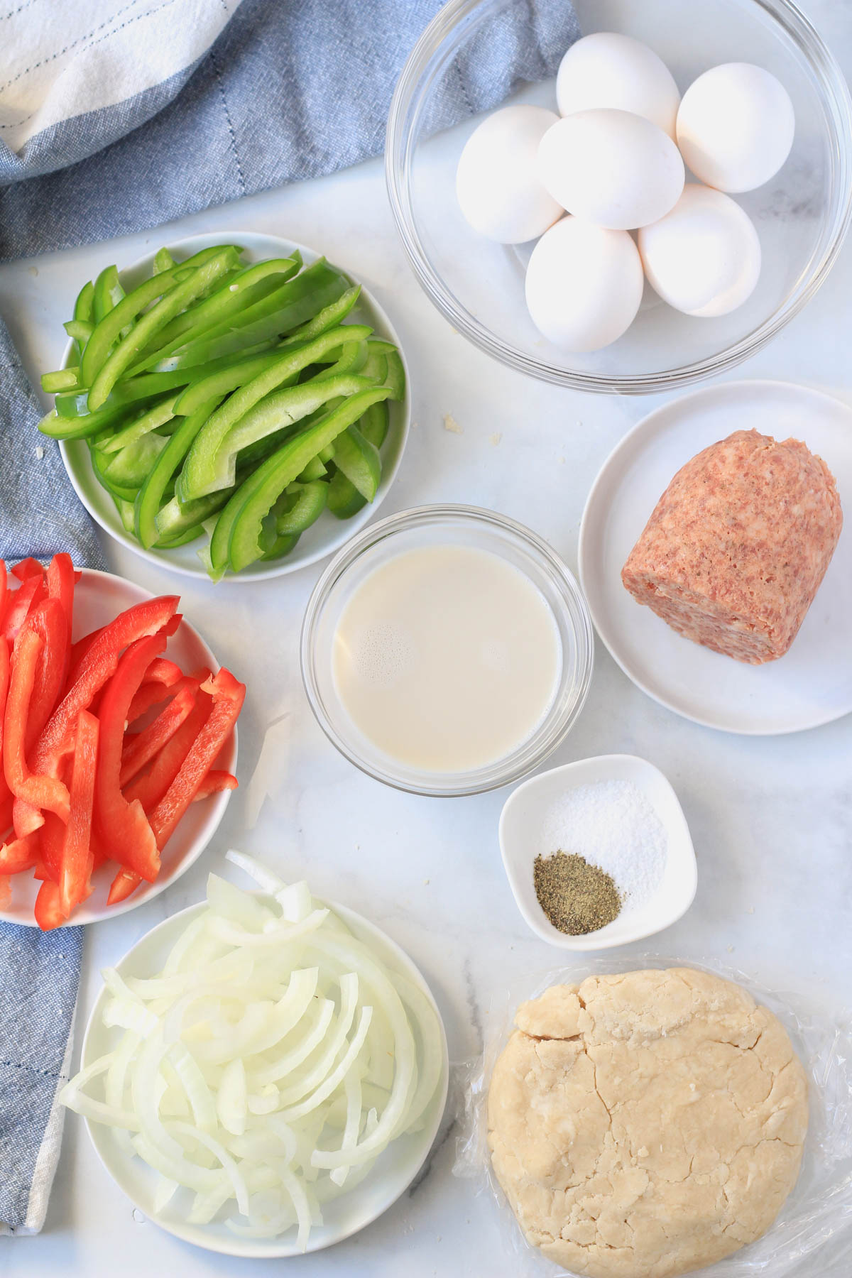 Ingredients for sausage and bell pepper quiche on a white counter.