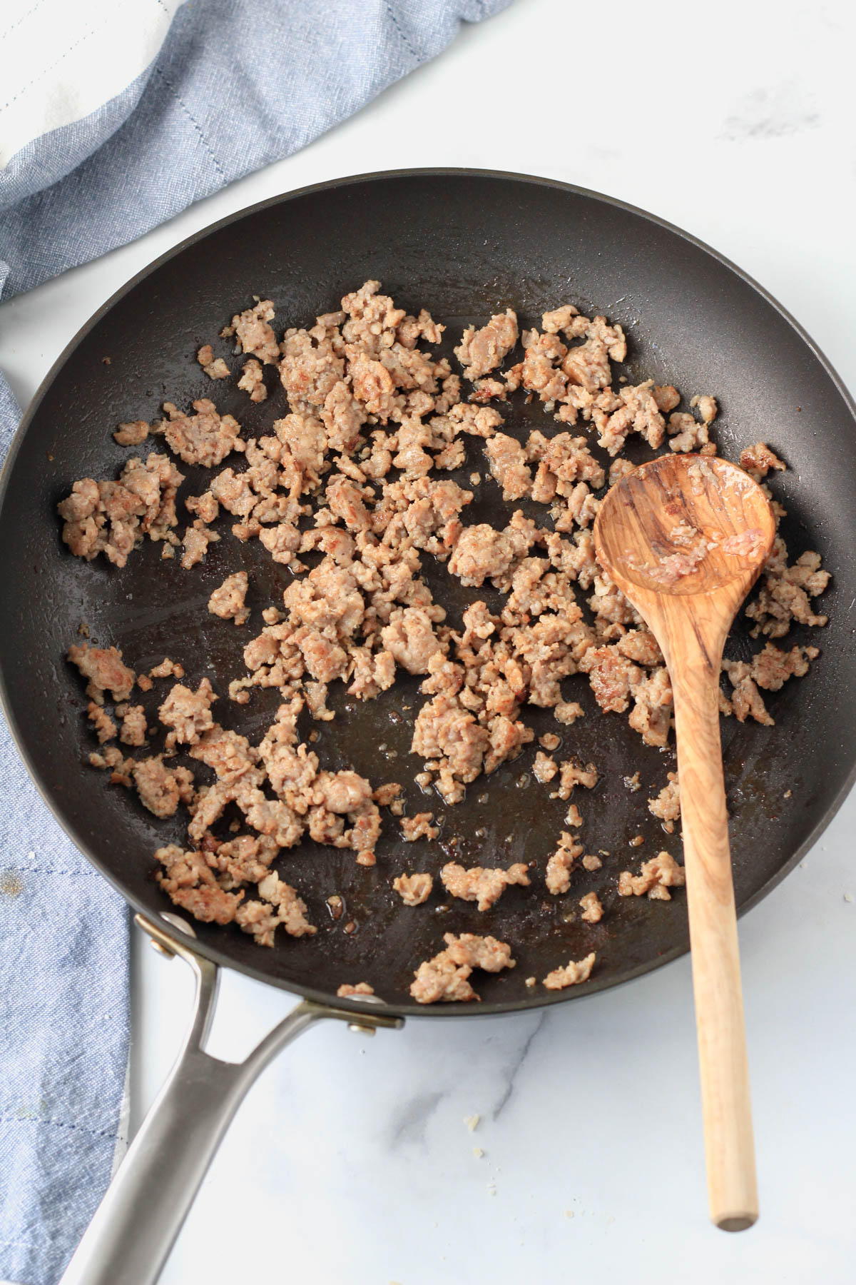 A non-stick skillet with breakfast sausage and a wooden spoon to the right.