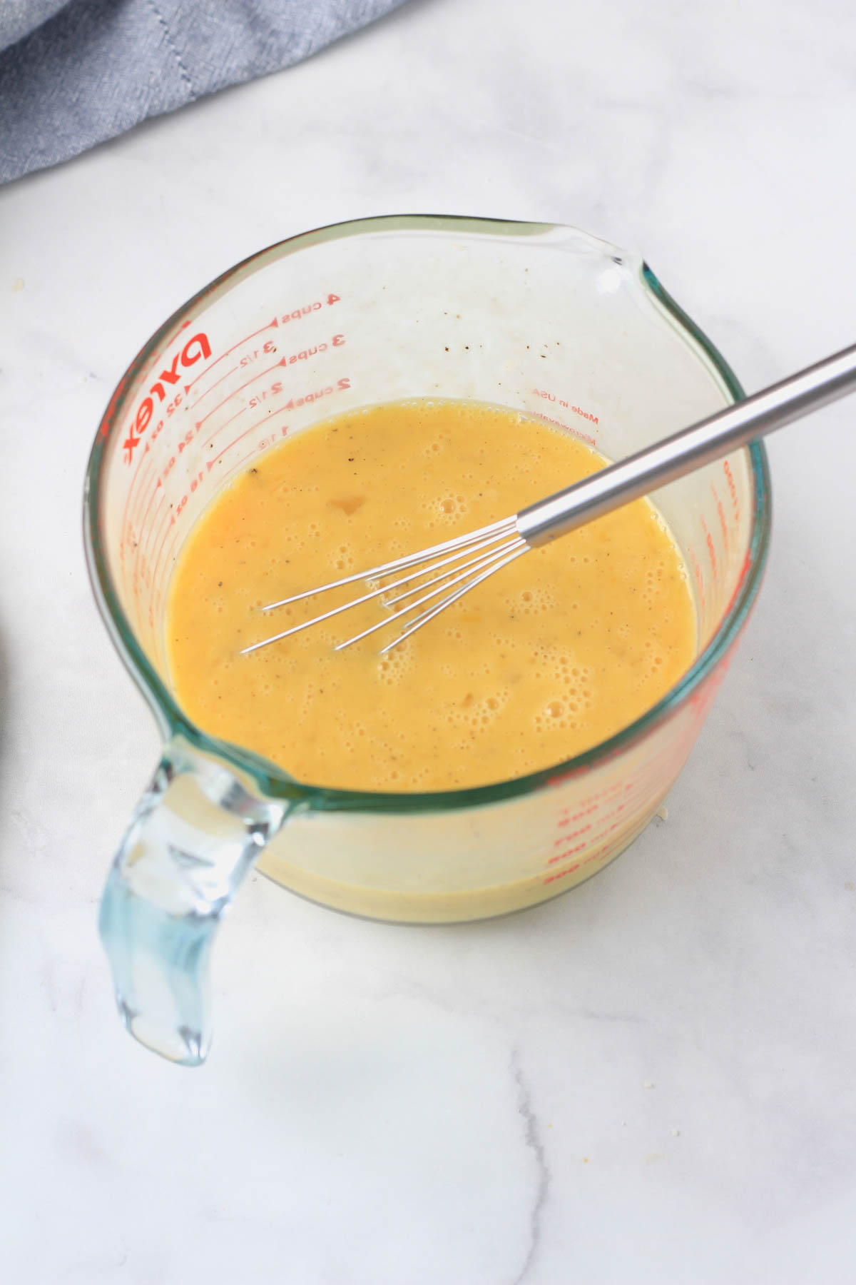 A large liquid measuring cup with a mini whisk and the egg mixture whisked together.