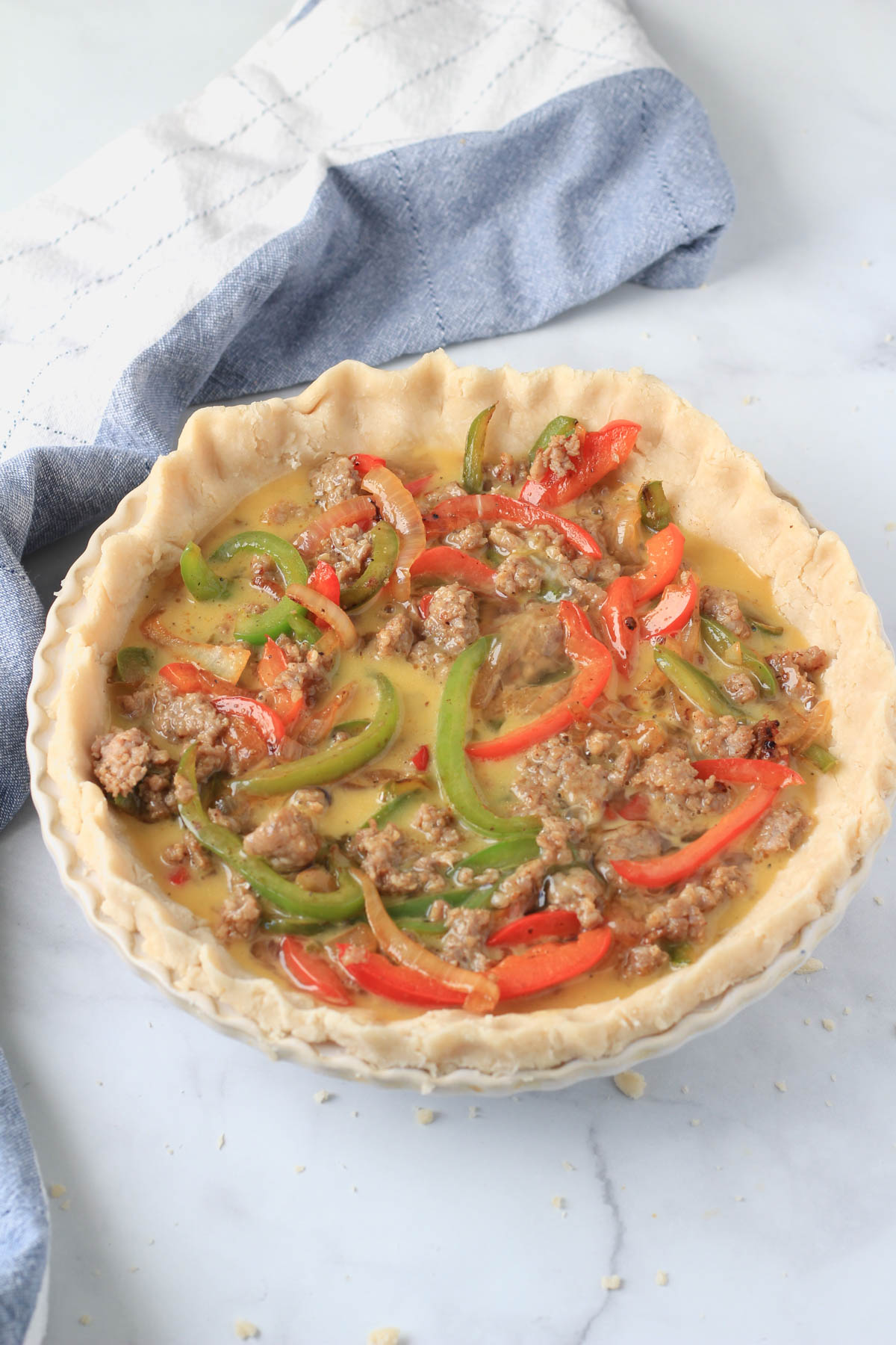 Sausage and bell pepper quiche on a white counter before baking.