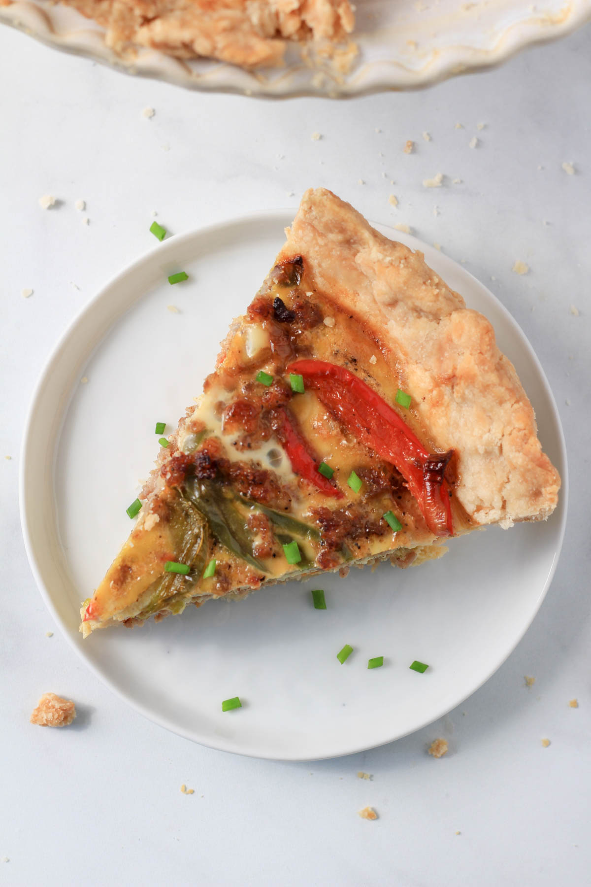 A white plate with a slice of sausage and bell pepper quiche topped with chive.