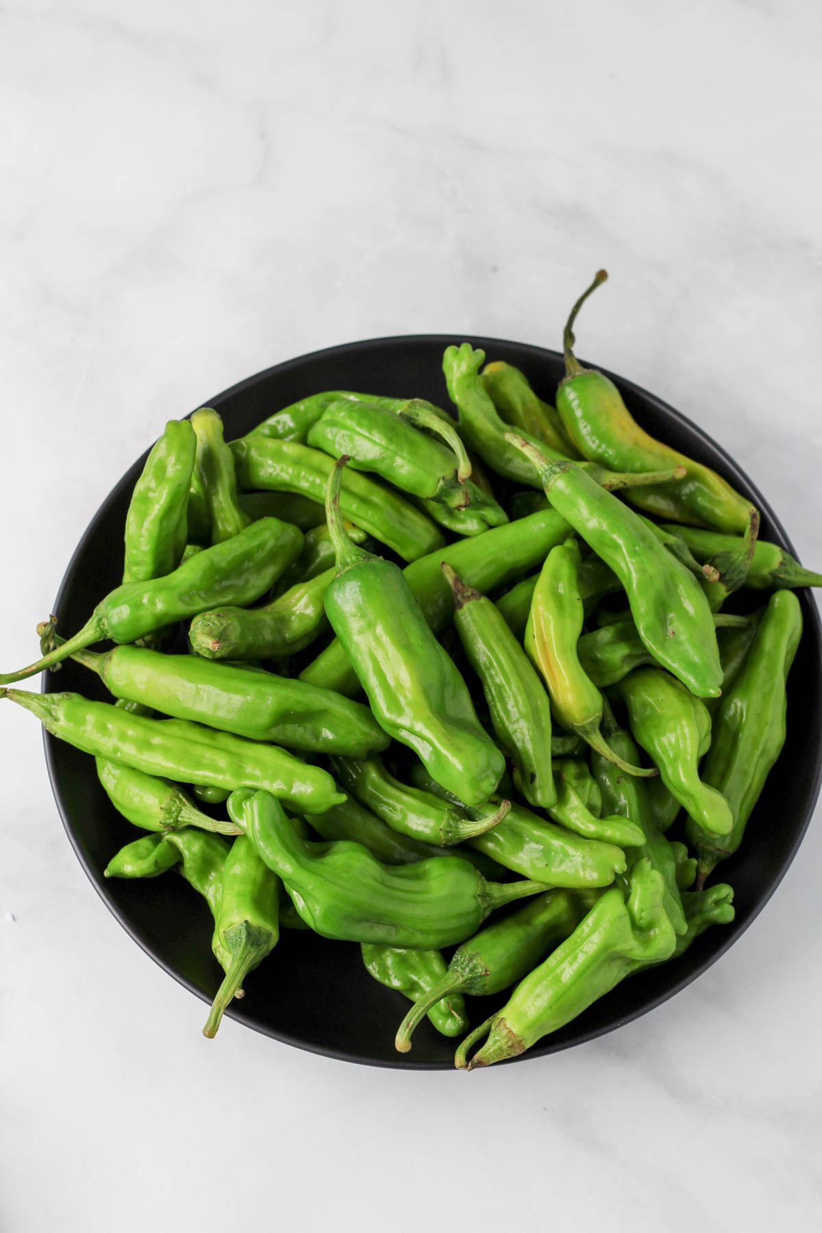 A black bowl with shishito peppers before cooking.