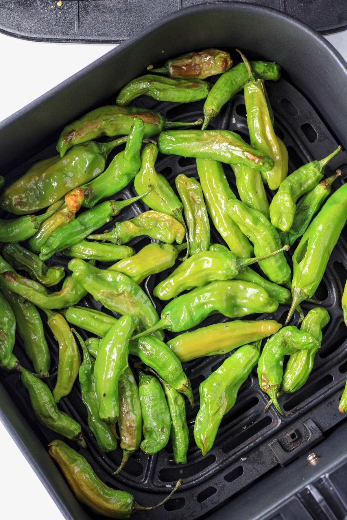 A basket of air fryer shishito peppers after they have cooked.