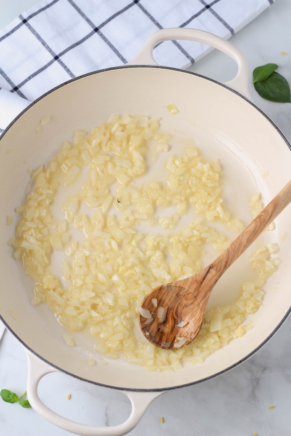 A white pan with garlic, onion, and melted vegan butter with a wooden spoon on the right side.