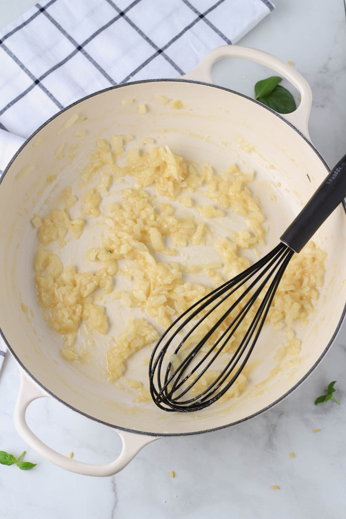 A white pan with a black whisk after mixing in the flour to make a roux.