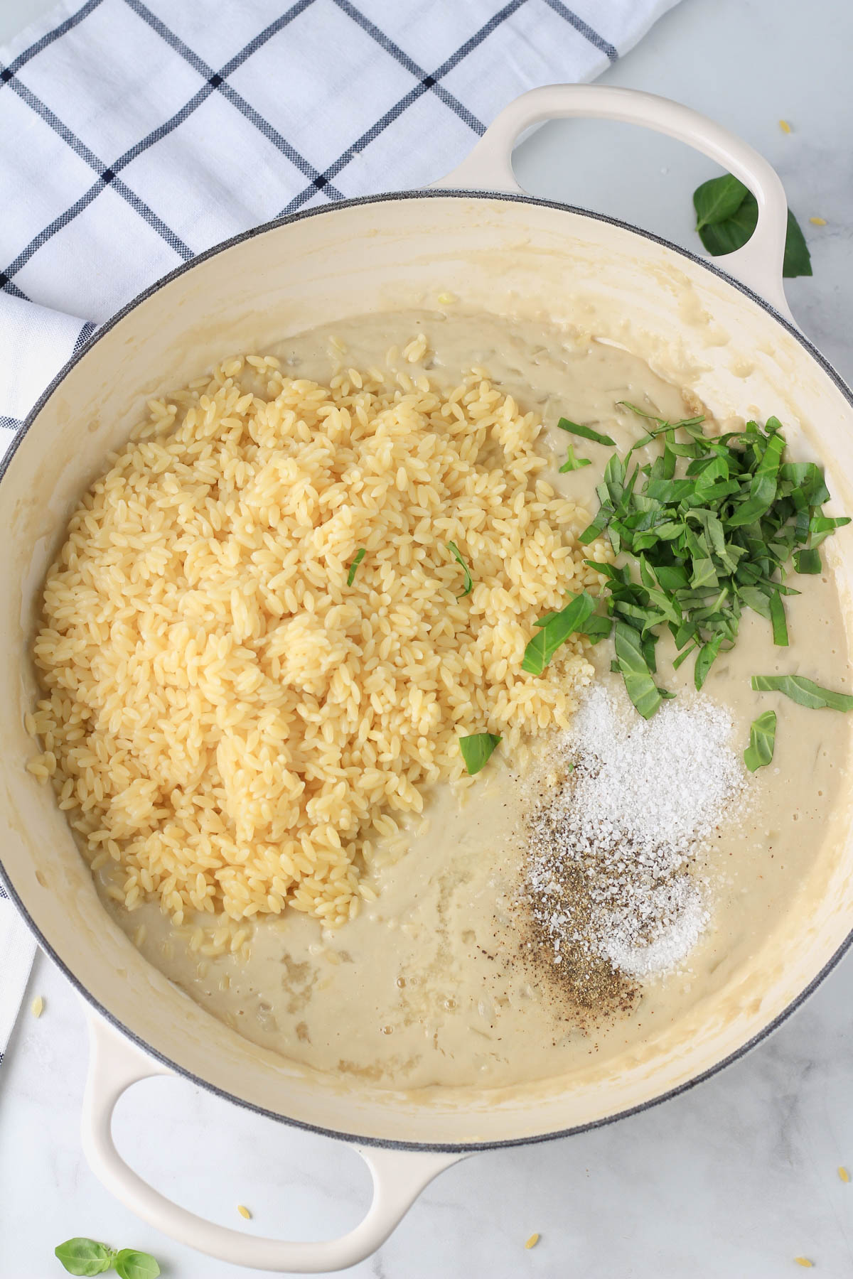 A white pan with creamy garlic sauce topped with orzo, seasoning, and basil.