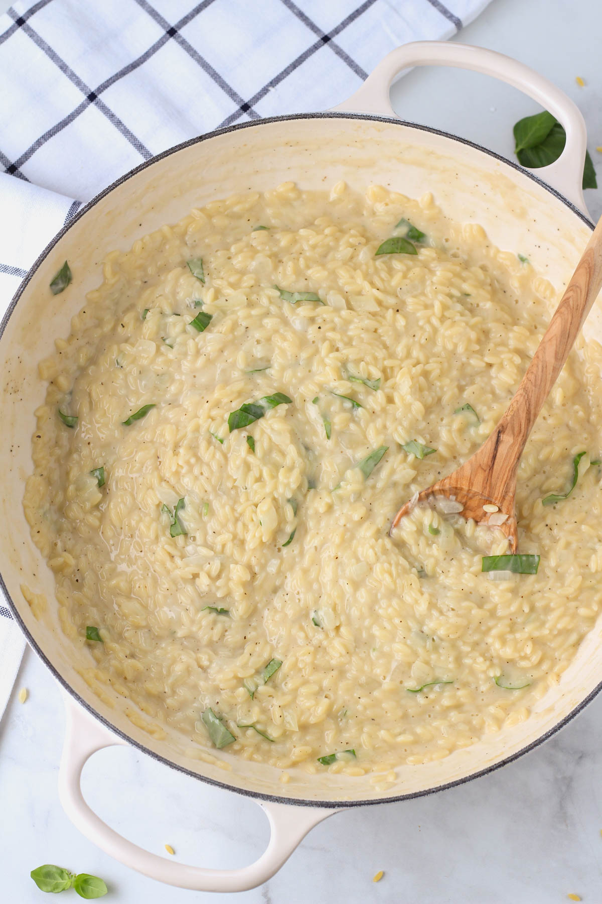 Creamy garlic orzo pasta in a white pan with a wooden spoon on the right side.