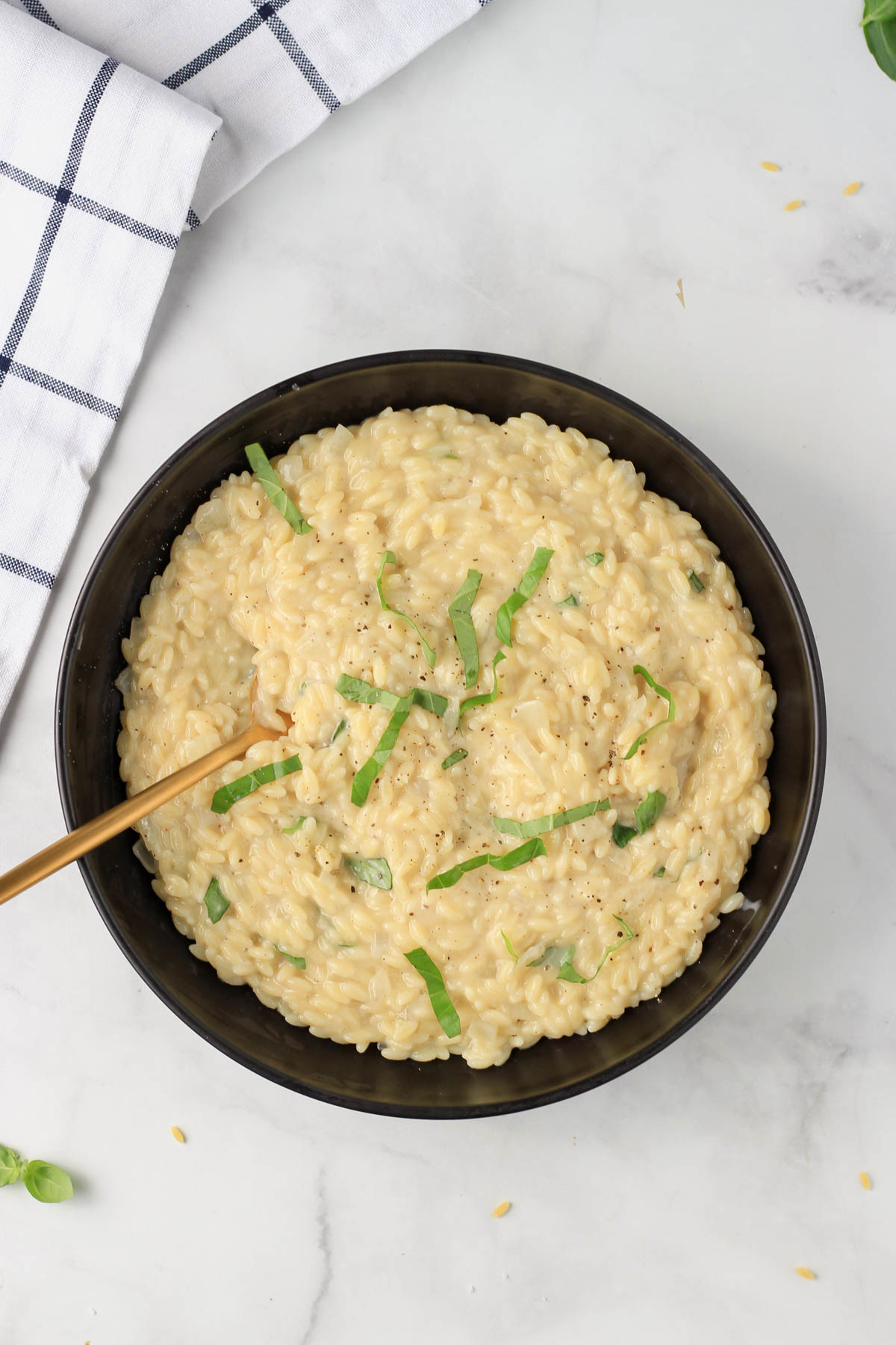 A black bowl filled with creamy garlic orzo pasta with a gold spoon in the left side of the bowl.