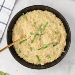 A close up of a bowl of creamy garlic orzo pasta with a gold spoon on the left.