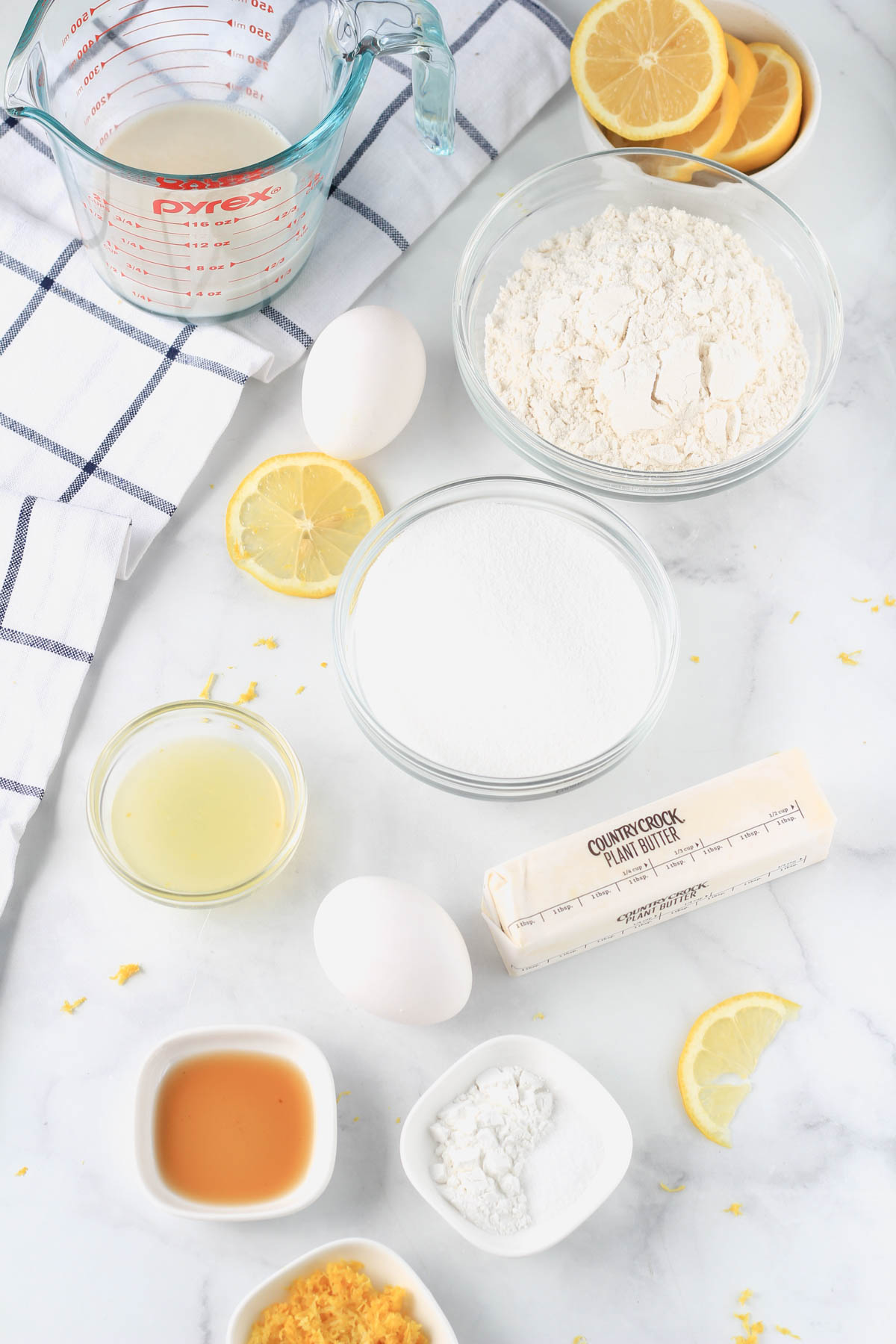 Ingredients for a lemon pound cake on a white counter with a blue and white towel to the left.