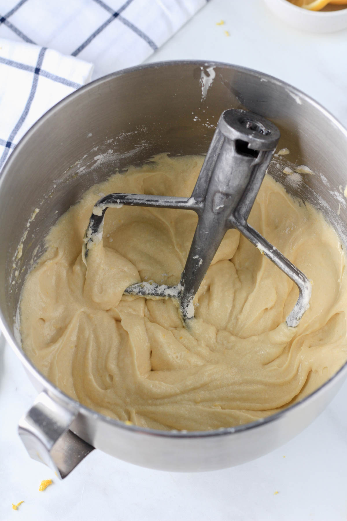 The lemon loaf batter after adding the liquid ingredients in a silver mixing bowl with the paddle attachment.