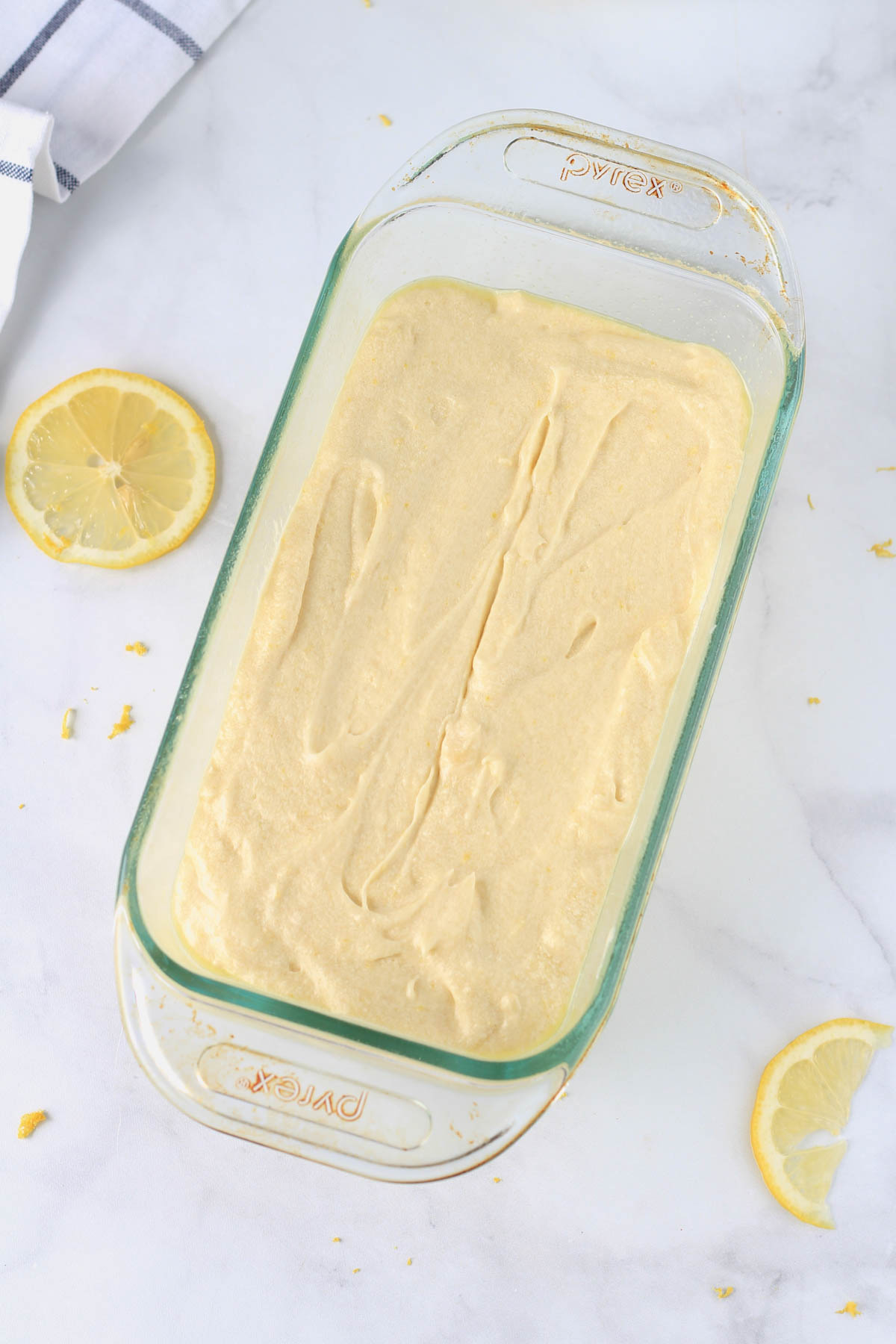 A glass loaf pan with the lemon cake batter on a white counter.
