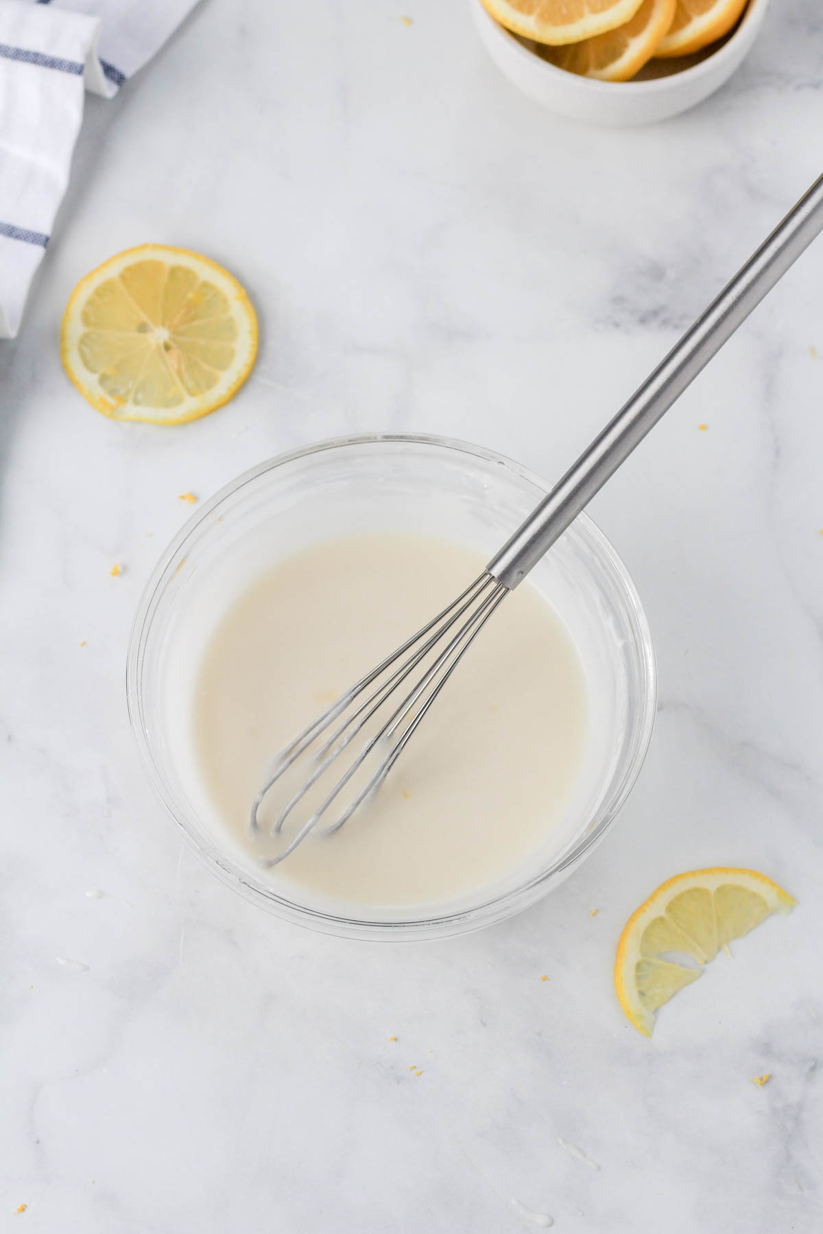 A small mixing bowl with a small whisk and the lemon icing mixed together.