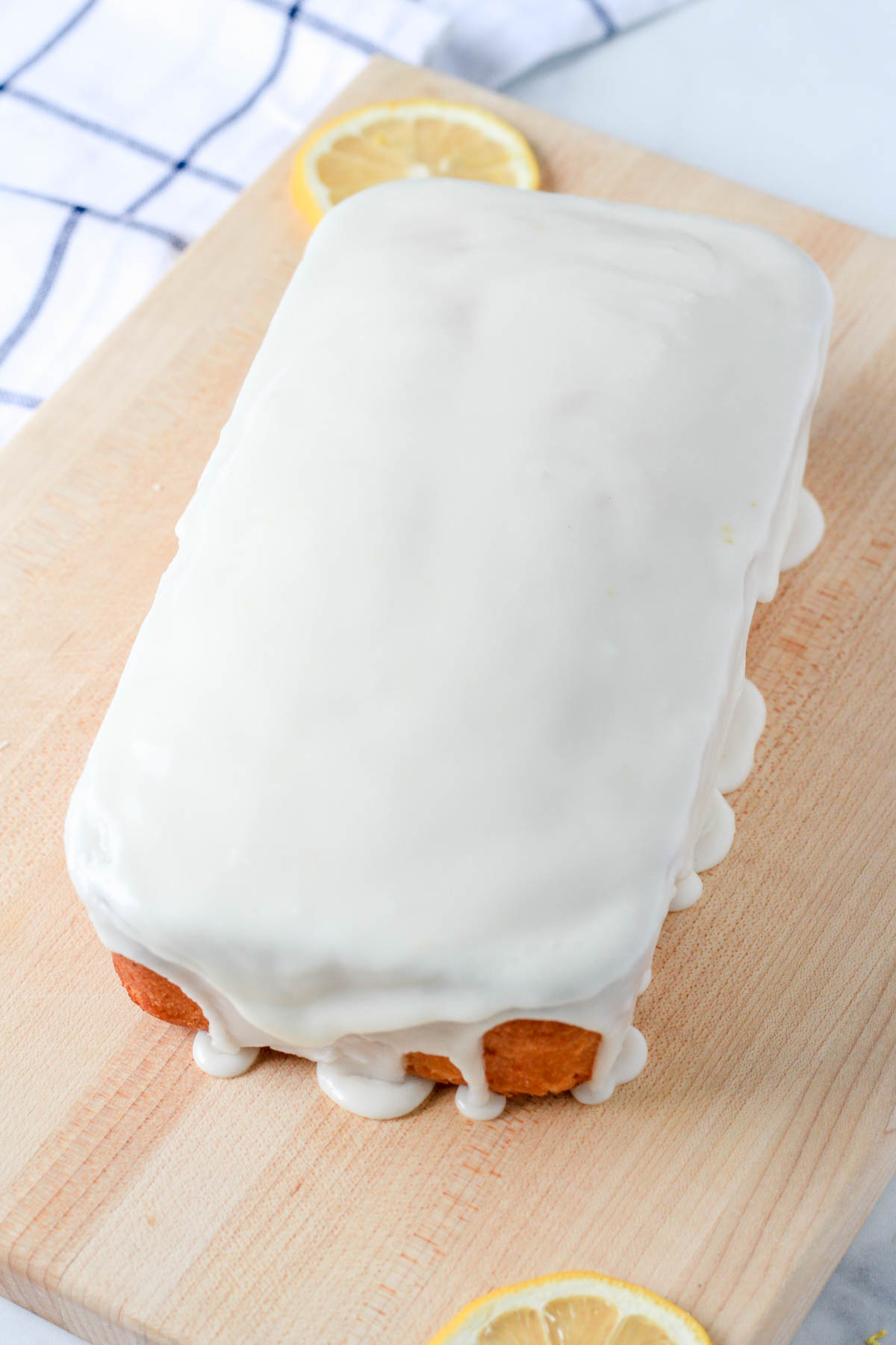 A wooden cutting board with an iced lemon loaf cake.