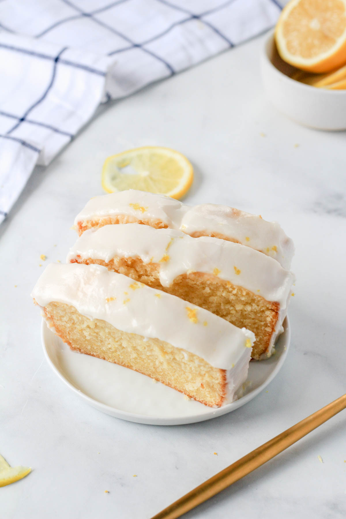 Three slices of dairy-free lemon loaf cake on a small white plate with a lemon slice in the back.