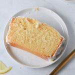 A small white plate with a slice of dairy-free lemon loaf cake.