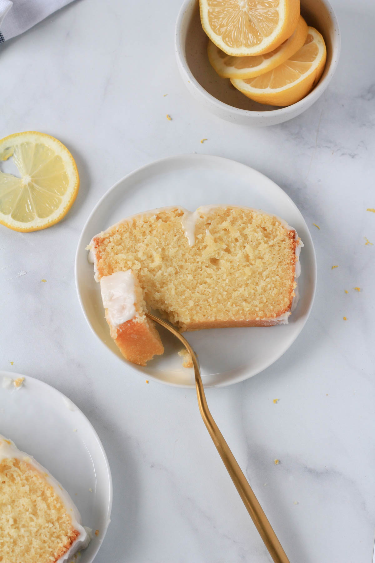 A slice of lemon loaf cake on a small white plate with a gold fork and a bite of cake on the fork.