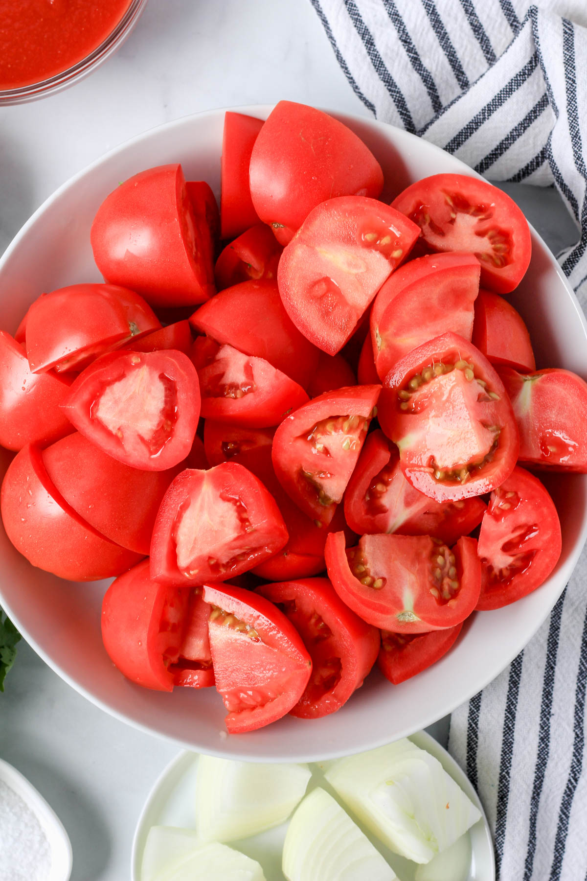 A white bowl with roma tomatoes that have been quartered.
