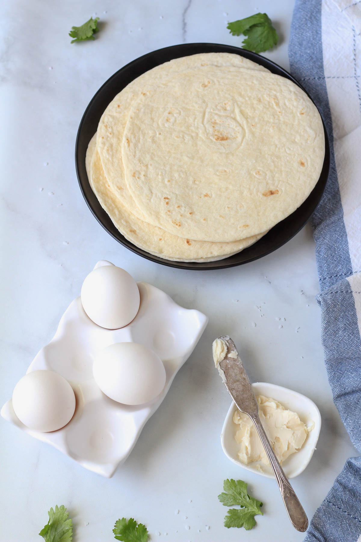 Ingredients for egg-a-dillas on a white counter with a blue and white striped towel to the right.