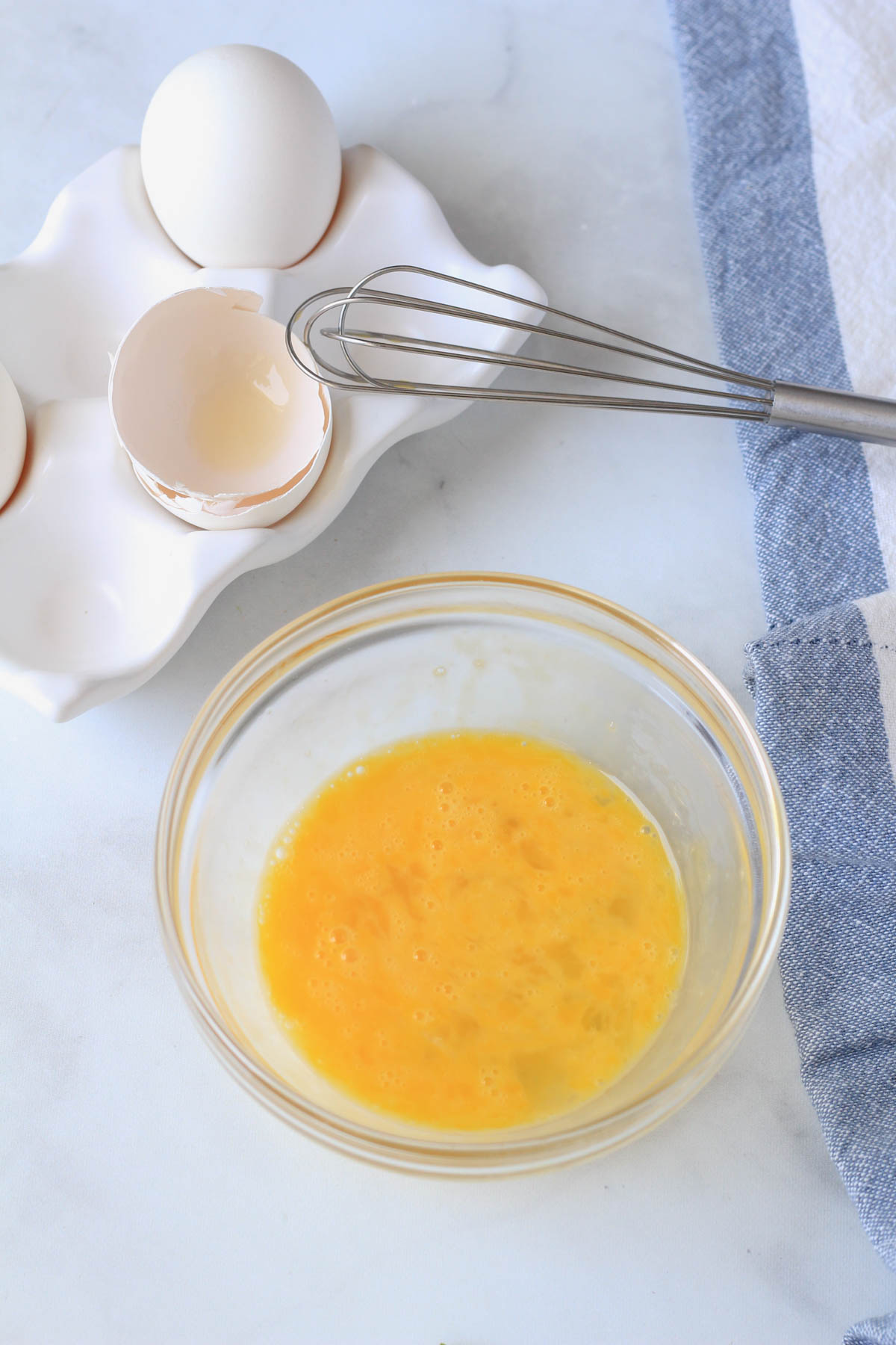 A small glass bowl with a scrambled egg and a small whisk in the back.