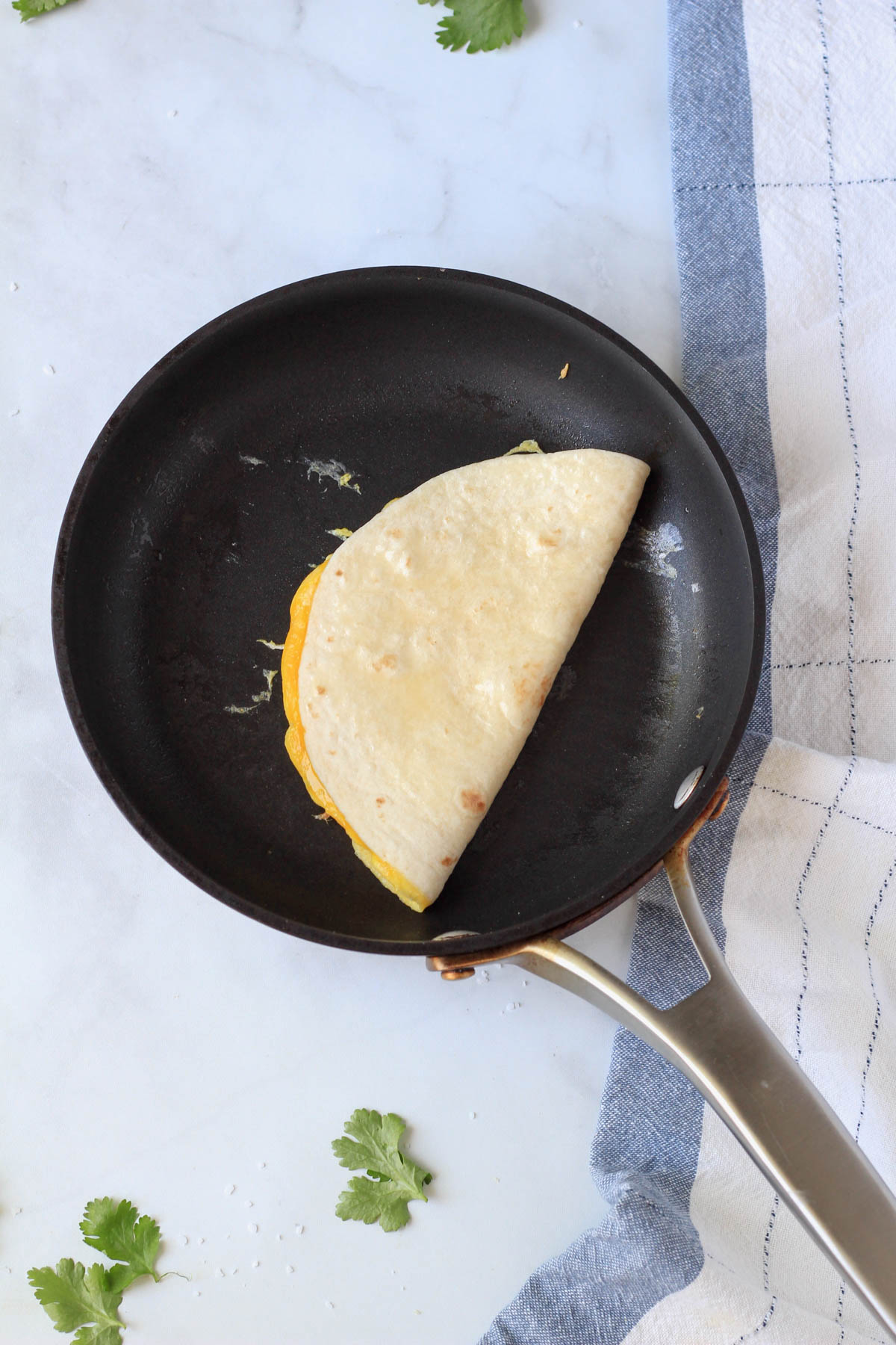 A small skillet with an egg-a-dilla cooking on one side.