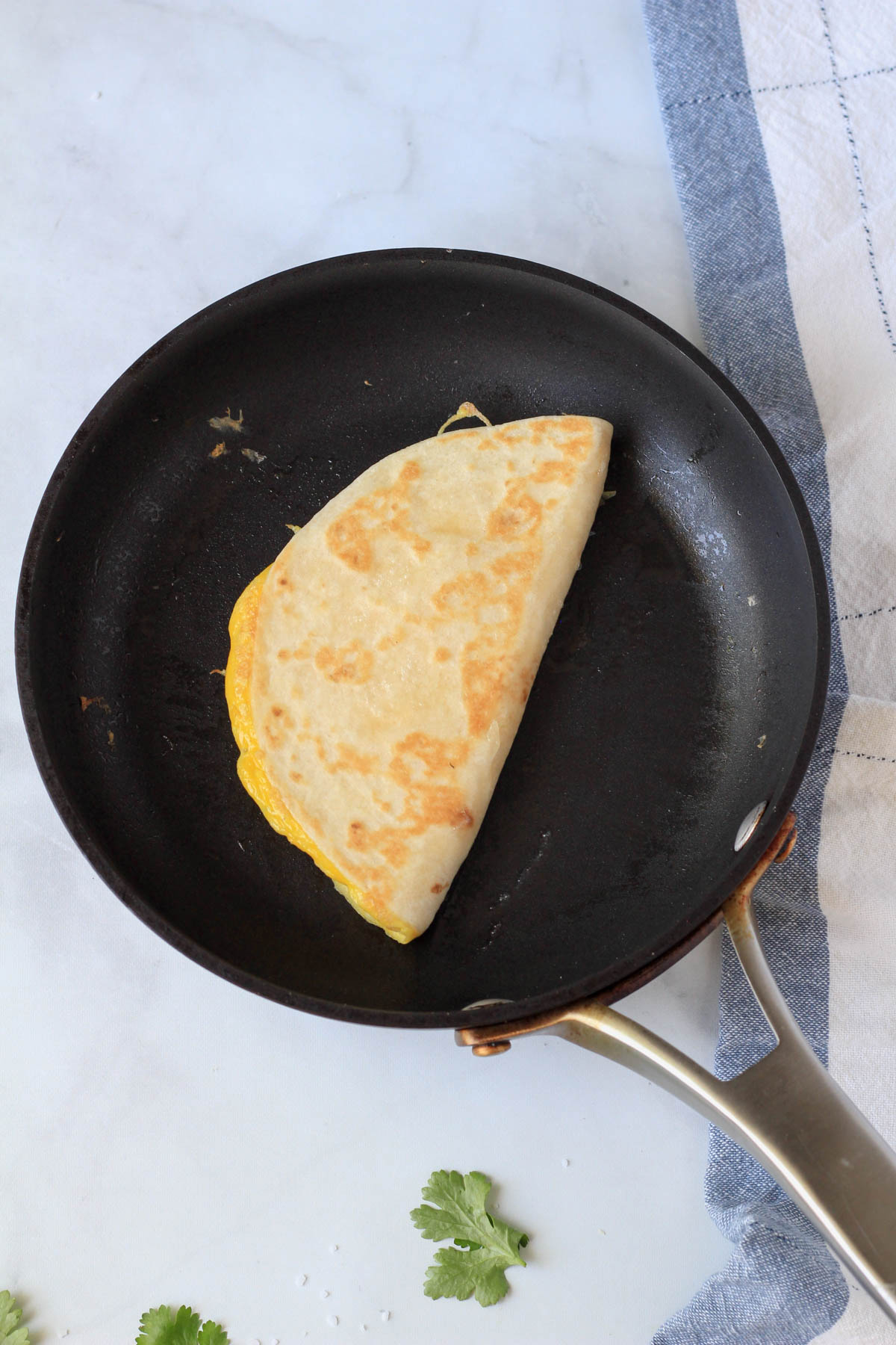 A small skillet with an egg-a-dilla cooking on the other side.