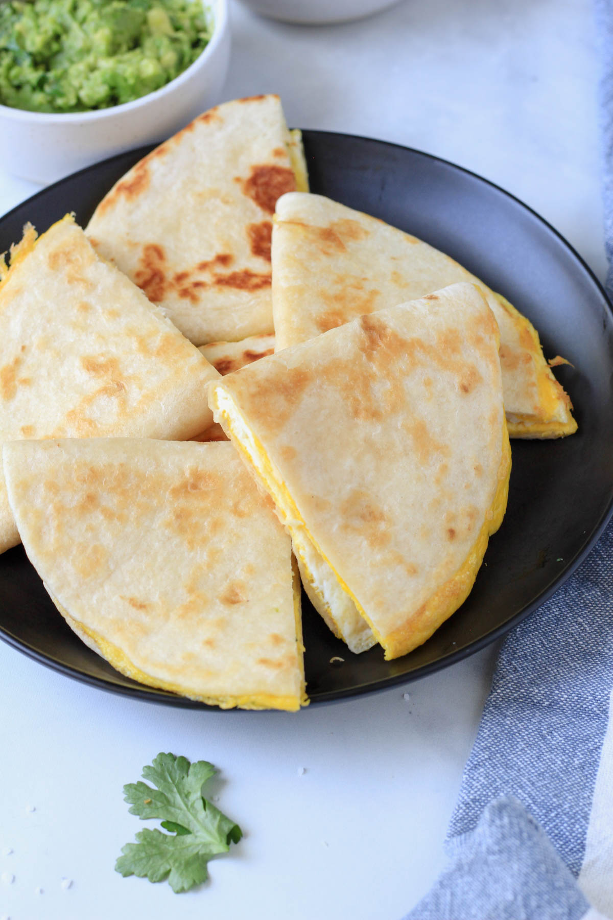 A plate of egg quesadilla wedges in a circle and some guacamole in the back left.