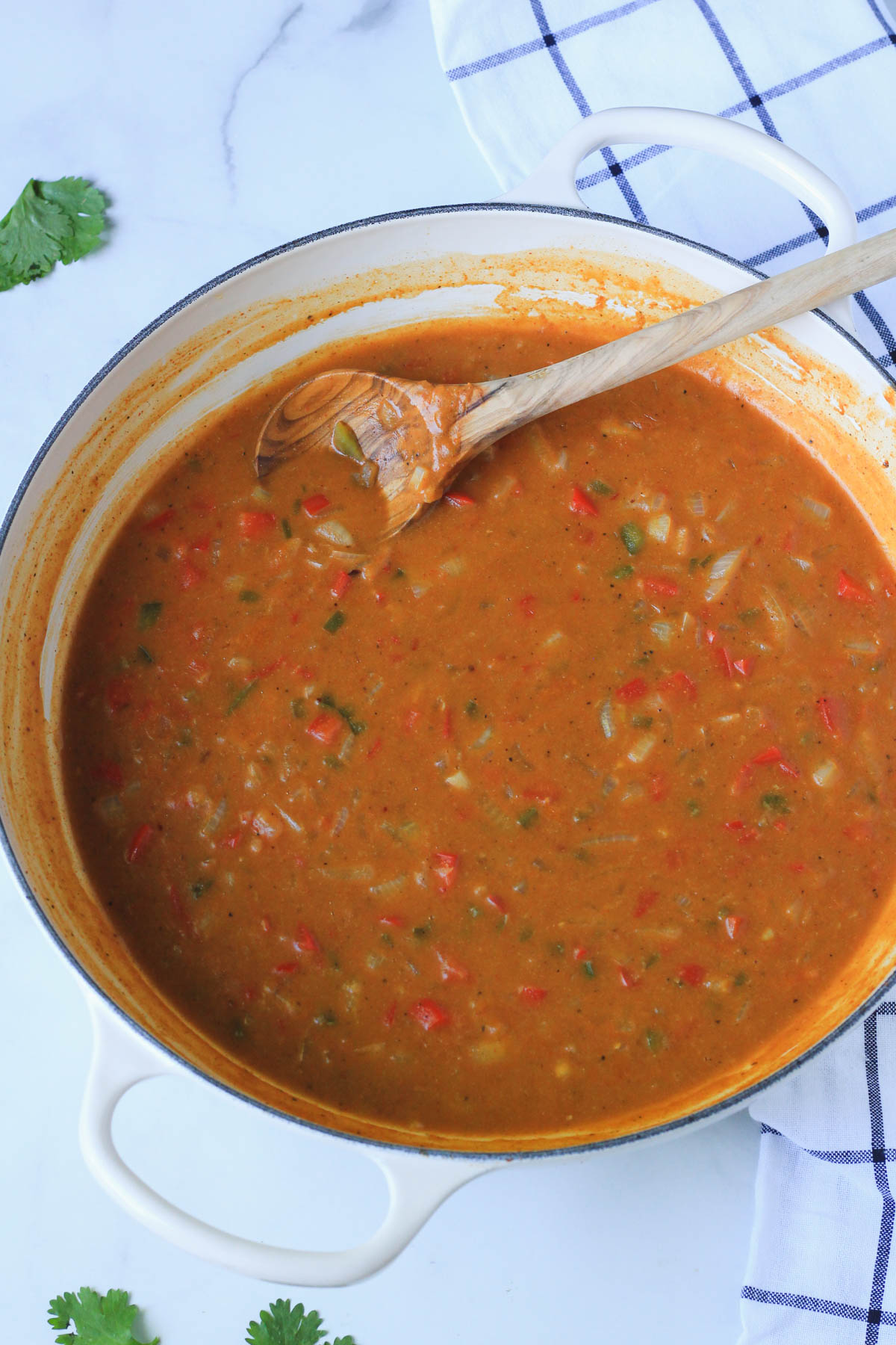 A creamy filling for the king ranch in a white skillet with a wooden spoon on a white counter.