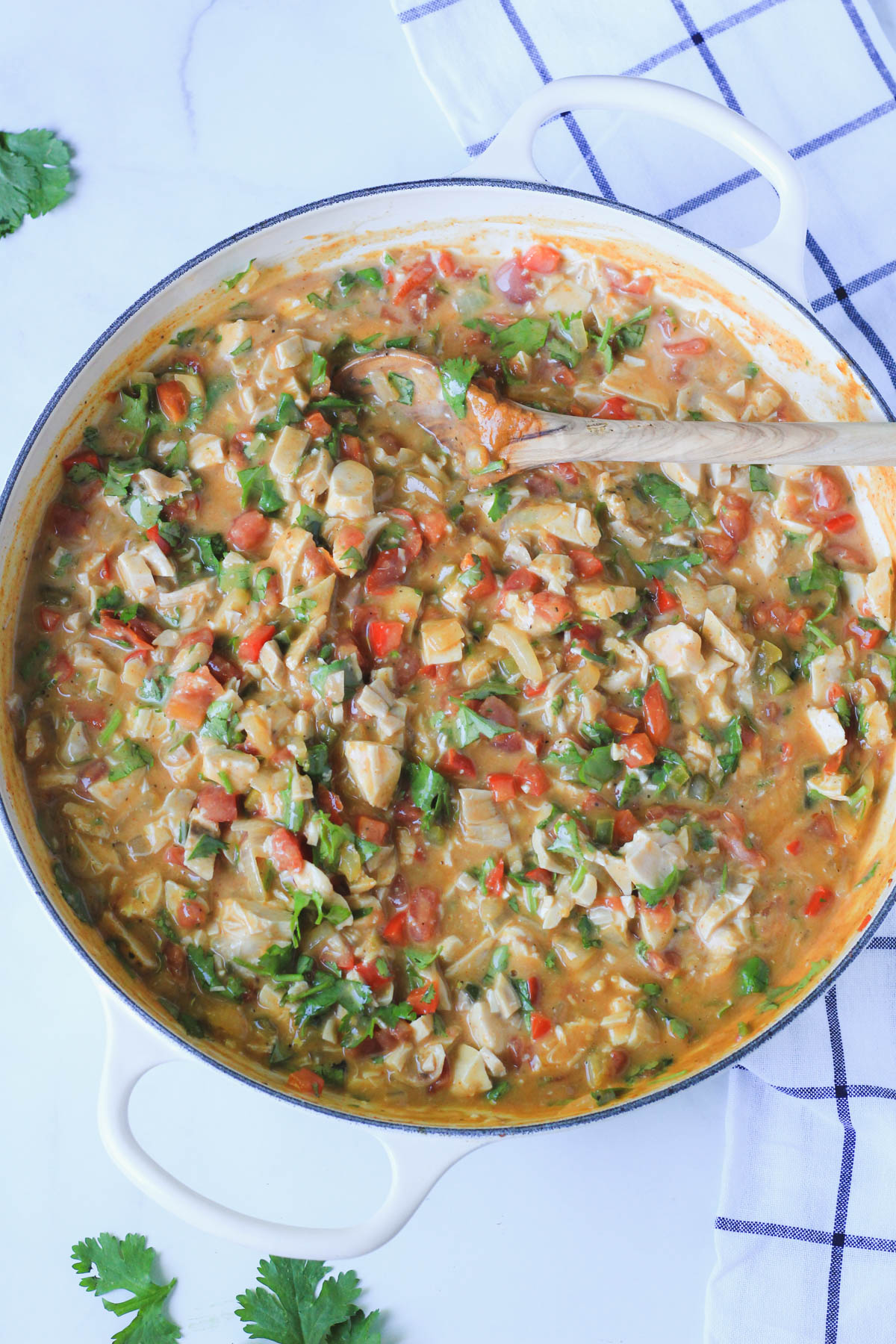 The king ranch casserole filling all mixed together in a white skillet with a wooden spoon on a white counter.