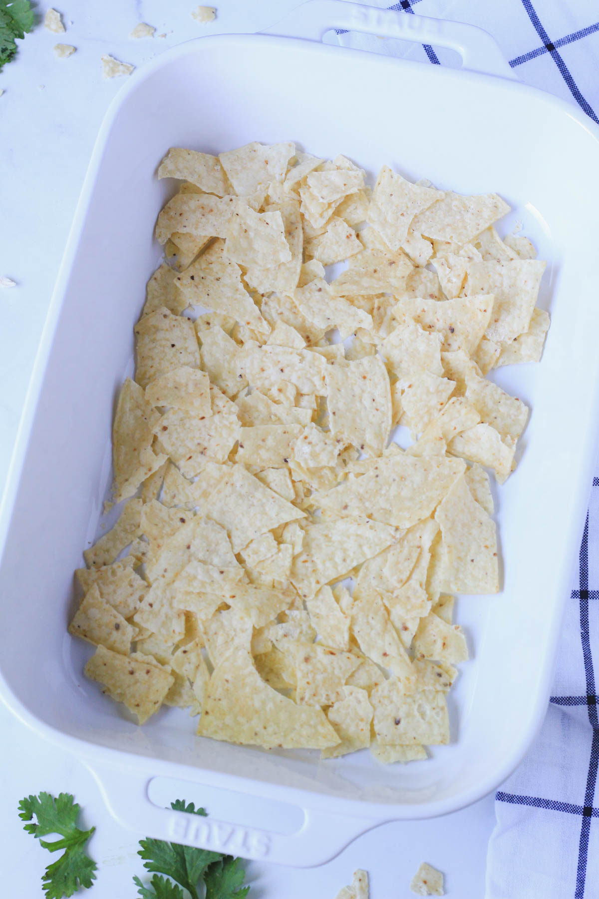A white casserole dish with a layer of tortilla chips at the bottom.