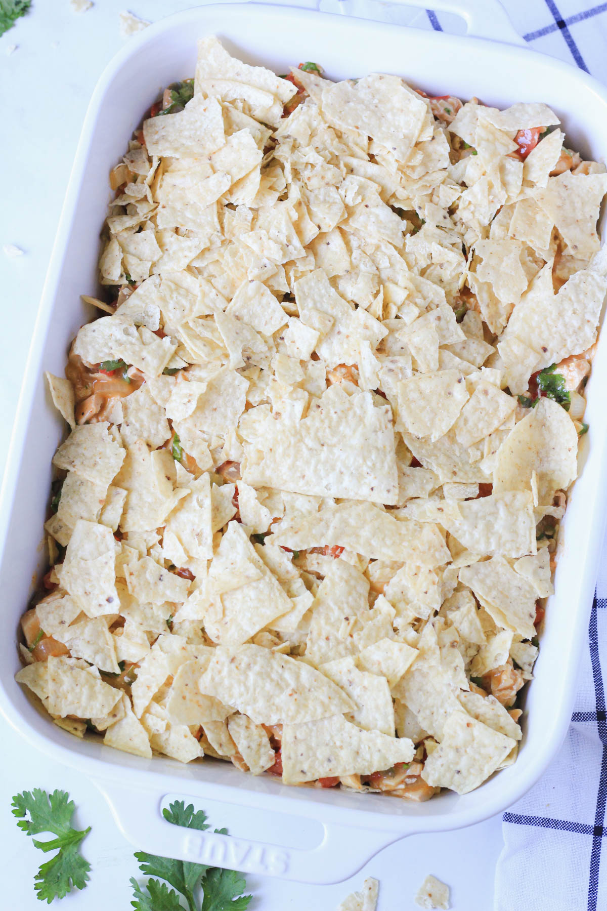 A layer of tortilla chips on top the king ranch casserole filling in a white baking dish.