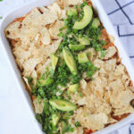 A white casserole pan with dairy-free king ranch chicken casserole topped with cilantro, avocado, and green onion.